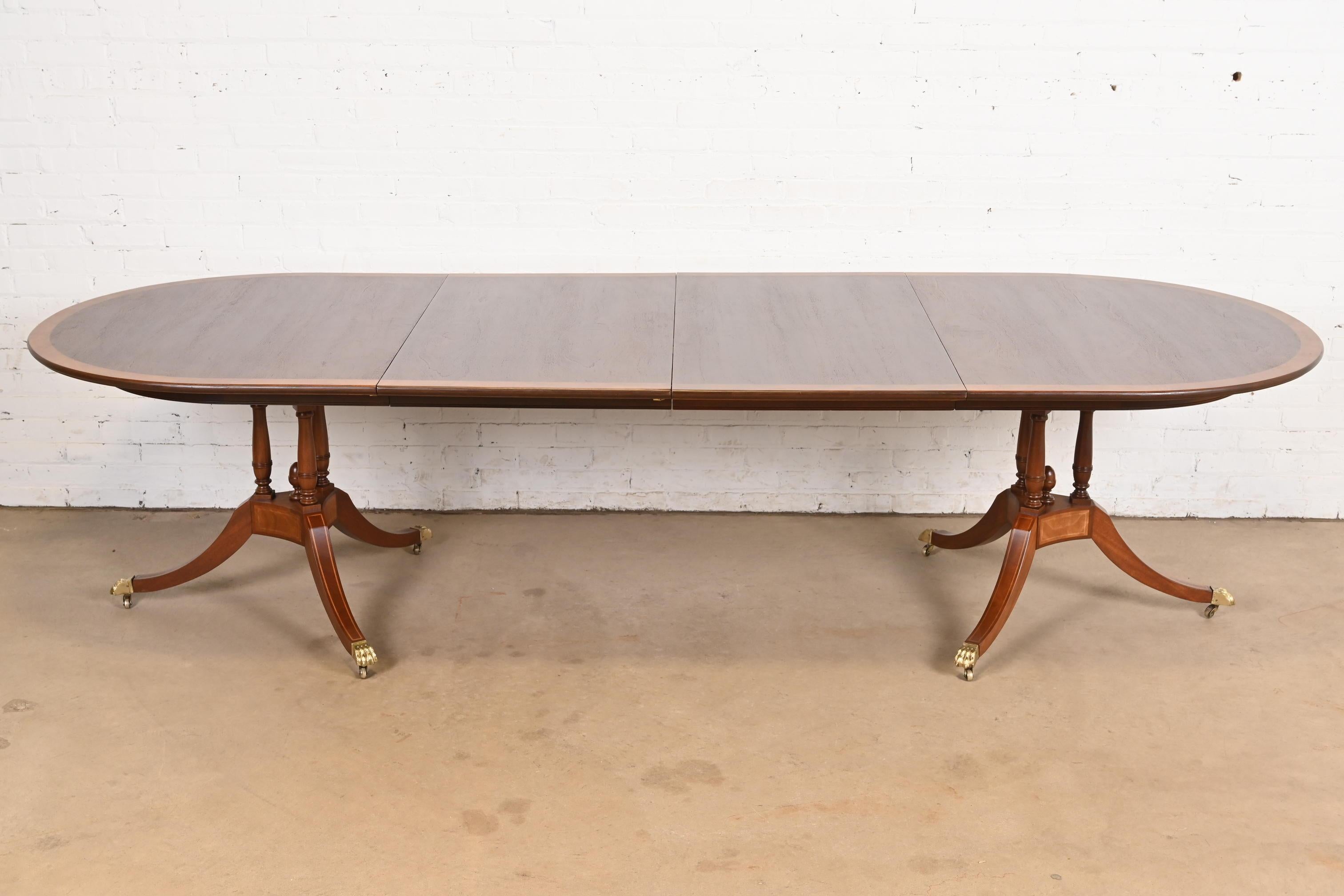An exceptional Georgian or Regency style double pedestal extension dining table

In the manner of Baker Furniture

USA, Circa 1960s

Gorgeous book-matched banded mahogany top, carved solid mahogany pedestals with inlaid satinwood, and brass-capped