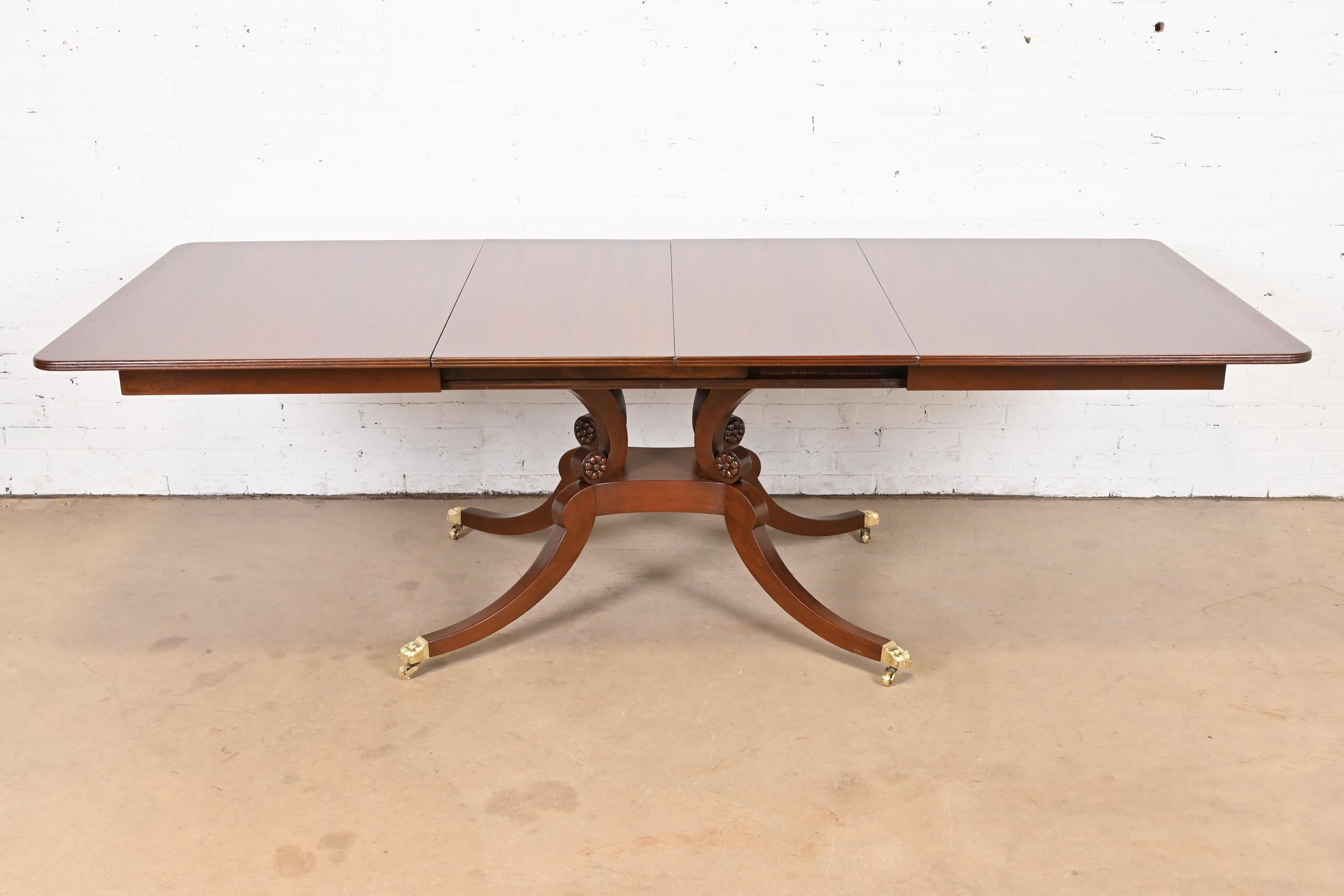 An exceptional Georgian or Regency style single pedestal extension dining table

In the manner of Baker Furniture

USA, Circa 1980s

Beautiful banded mahogany top, with carved solid mahogany pedestal, brass-capped paw feet on brass casters, and