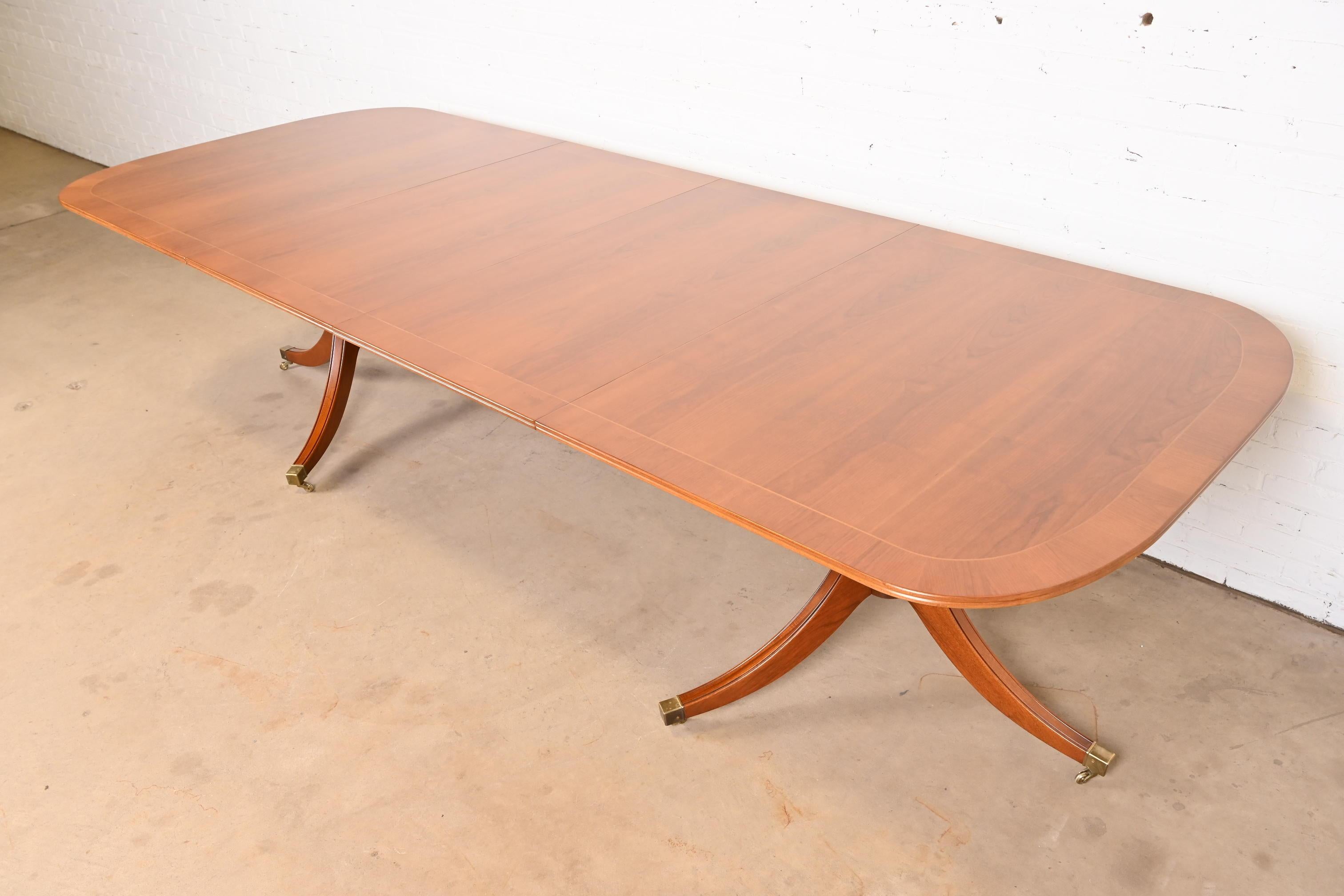 An exceptional Georgian or Regency style extension double pedestal dining table

In the manner of Baker Furniture

USA, Circa 1980s

Gorgeous book-matched banded cherry wood, with satinwood string inlay, carved pedestals, brass-capped feet, and