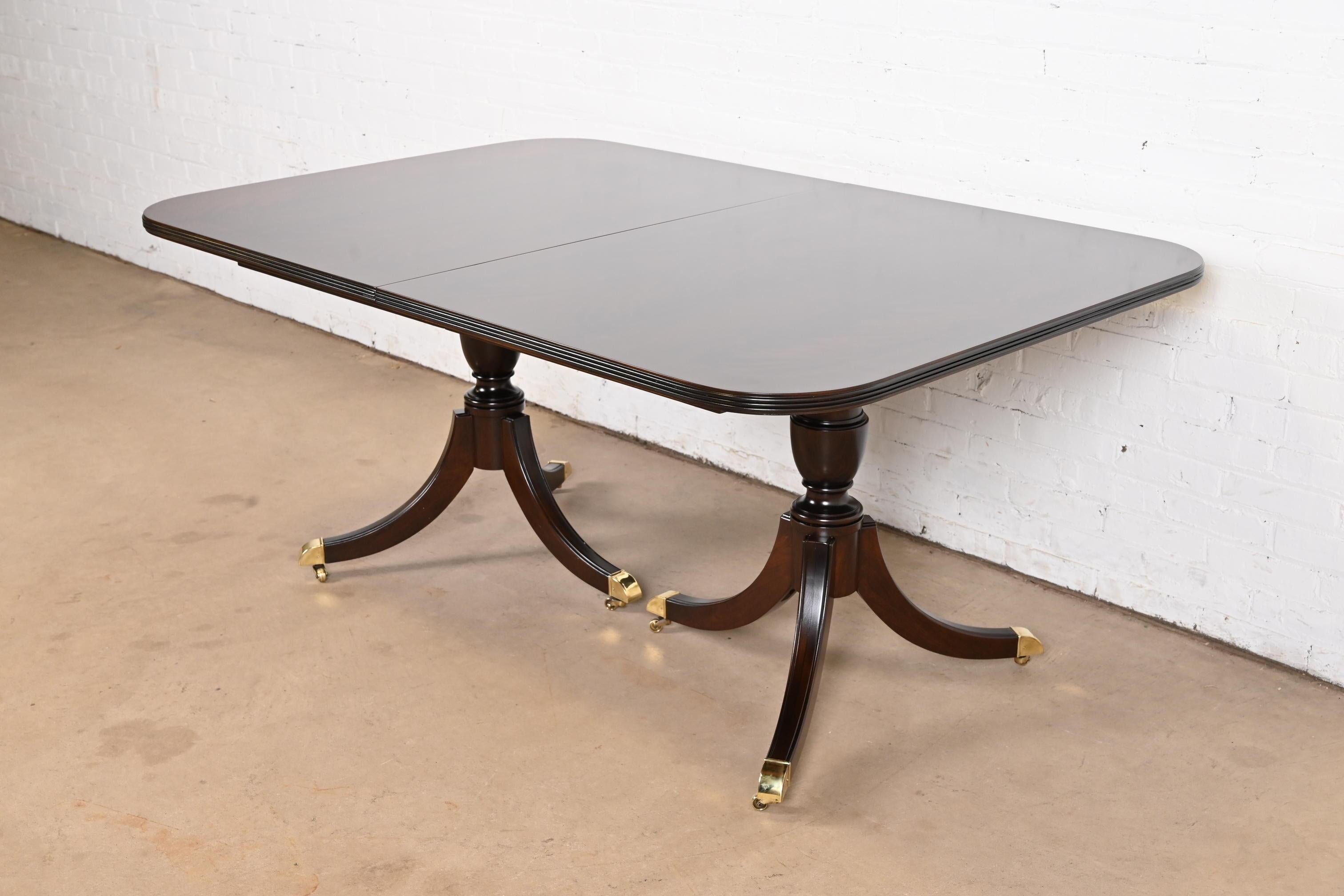 An exceptional Georgian or Regency style double pedestal dining table

In the manner of Baker Furniture

USA, Circa Mid-20th Century

Gorgeous figural flame mahogany top, with satinwood string inlay and yew wood banding, carved solid mahogany