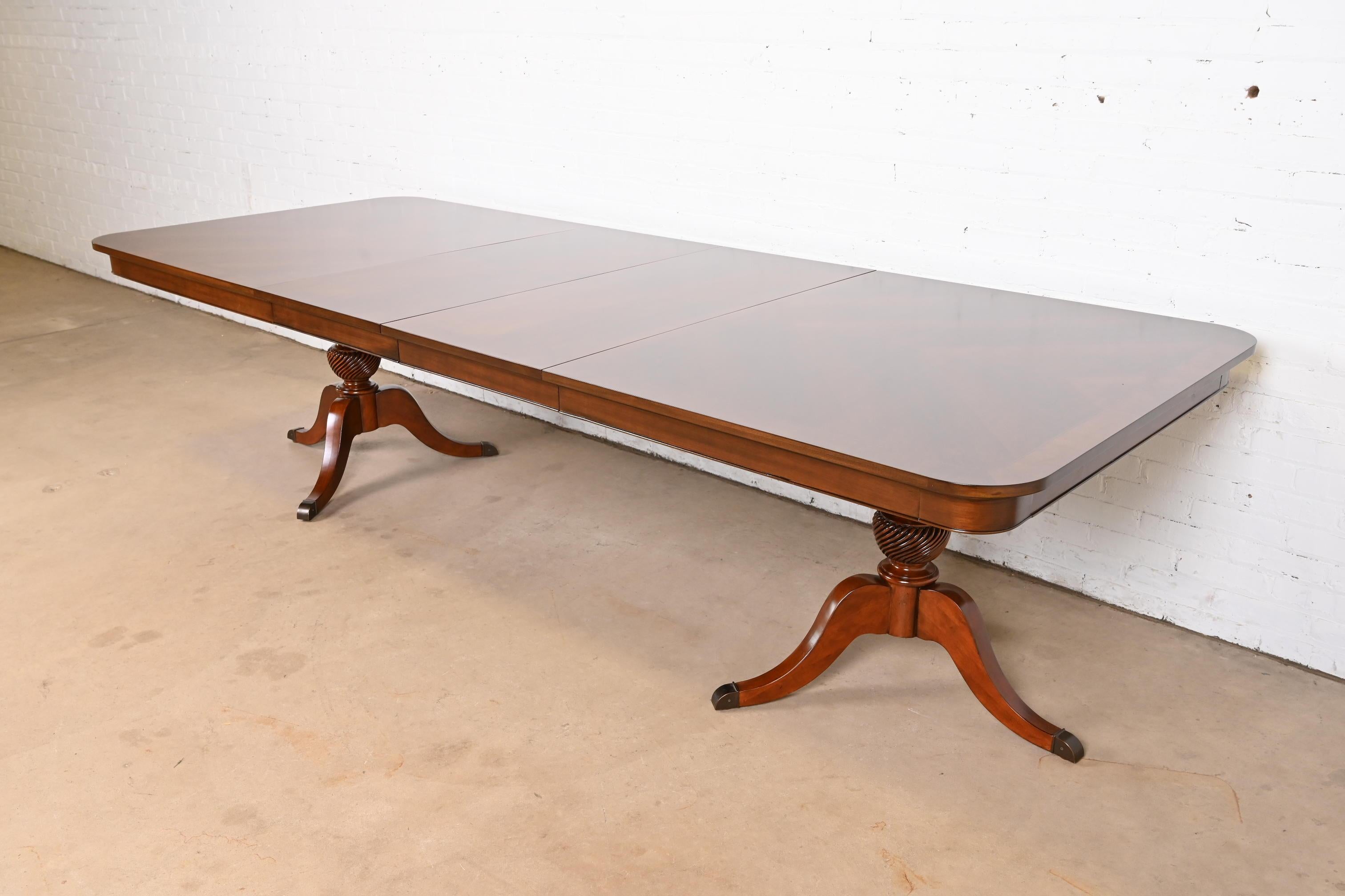 Exceptionnelle table à manger à rallonge à double piédestal de style Géorgien ou Régence.

À la manière des meubles Baker

USA, Circa 1980

Magnifique plateau en cerisier marqueté assorti à un livre, avec des piédestaux en cerisier massif sculpté et