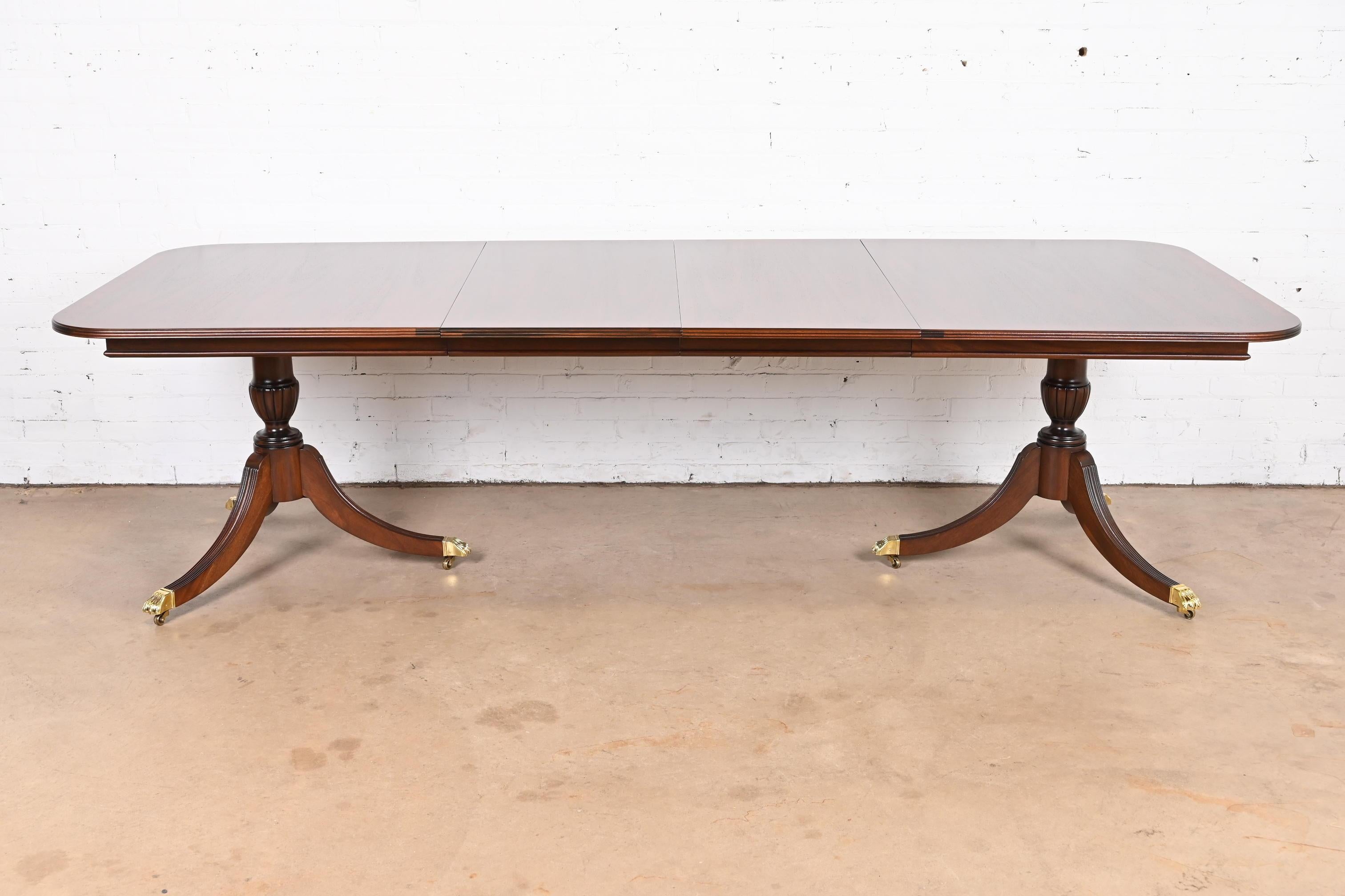 An exceptional Georgian or Regency style double pedestal extension dining table

In the manner of Baker Furniture

USA, Circa 1980s

Gorgeous book-matched banded mahogany top, with carved solid mahogany pedestals, brass-capped paw feet, and brass