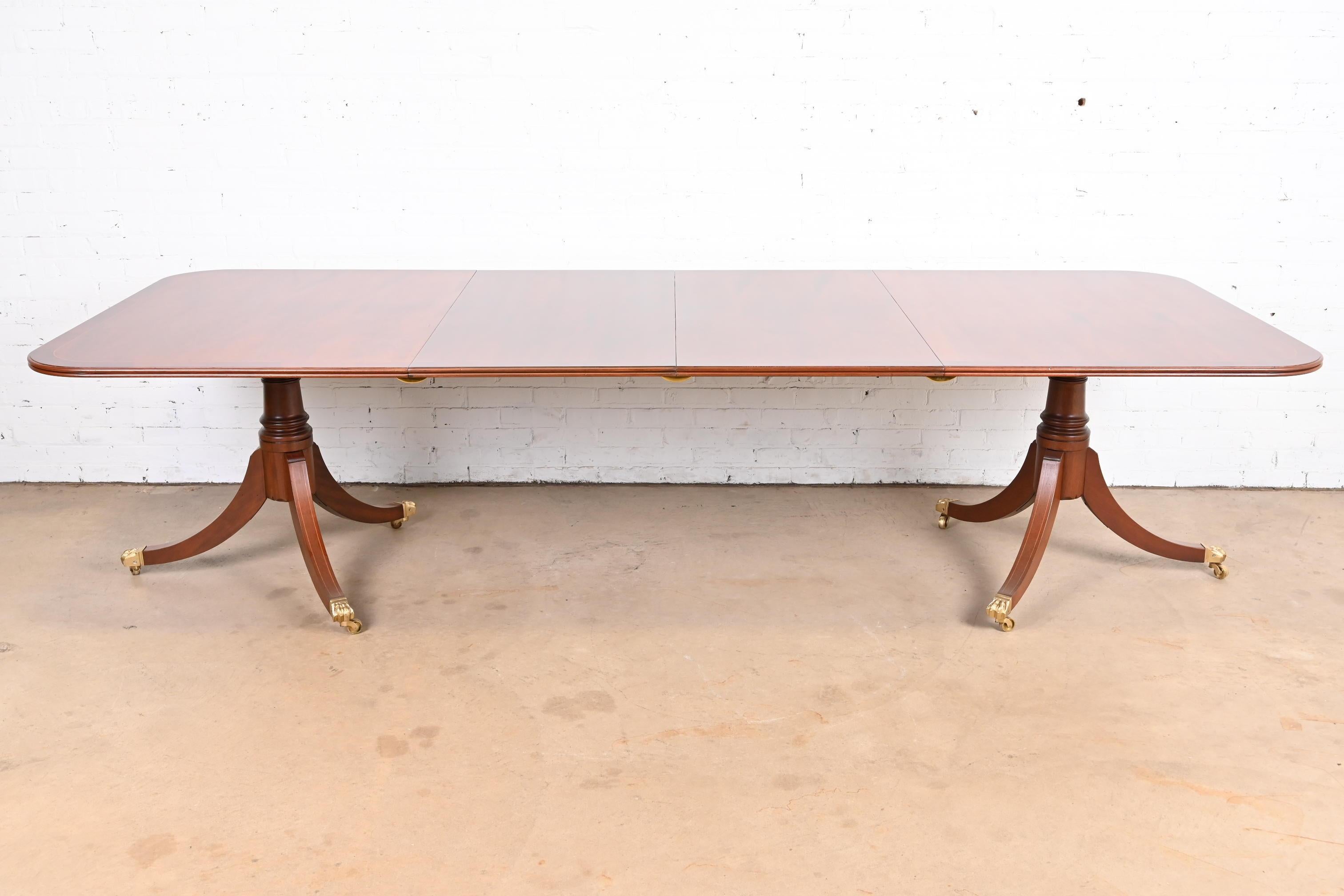 A gorgeous Georgian or Regency style double pedestal extension dining table

In the manner of Baker Furniture

USA, Circa 1960s

Beautiful banded mahogany, with satinwood string inlay, carved solid mahogany pedestals, and brass-capped paw feet on