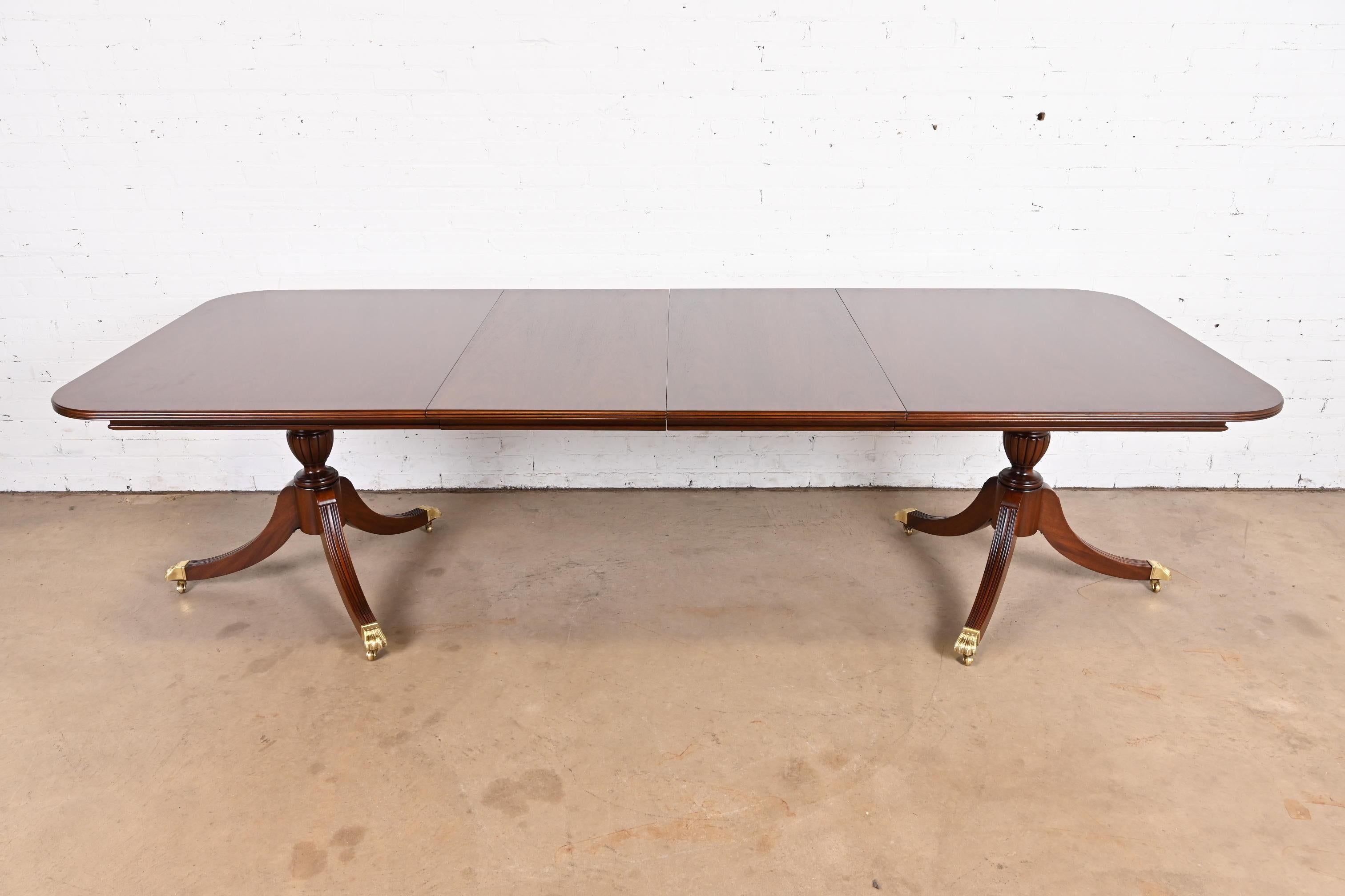 A gorgeous Georgian or Regency style double pedestal extension dining table

In the manner of Baker Furniture

USA, Circa 1980s

Beautiful book-matched banded mahogany, with carved solid mahogany pedestals, and brass-capped paw feet on brass