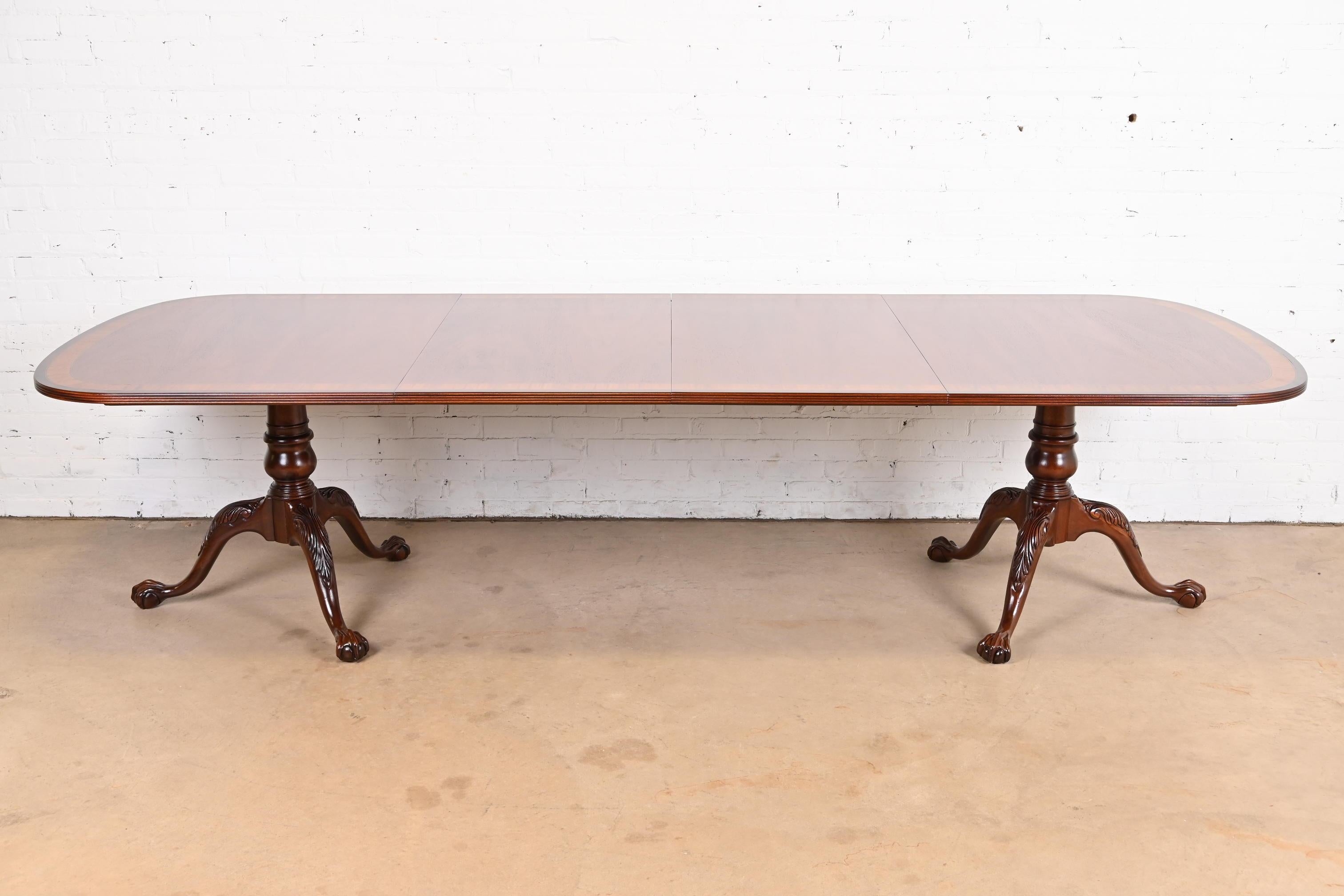 An exceptional Georgian or Chippendale style double pedestal extension dining table

In the manner of Baker Furniture

USA, Circa Late 20th Century

Gorgeous book-matched mahogany, with satinwood banding, and carved solid mahogany pedestals with