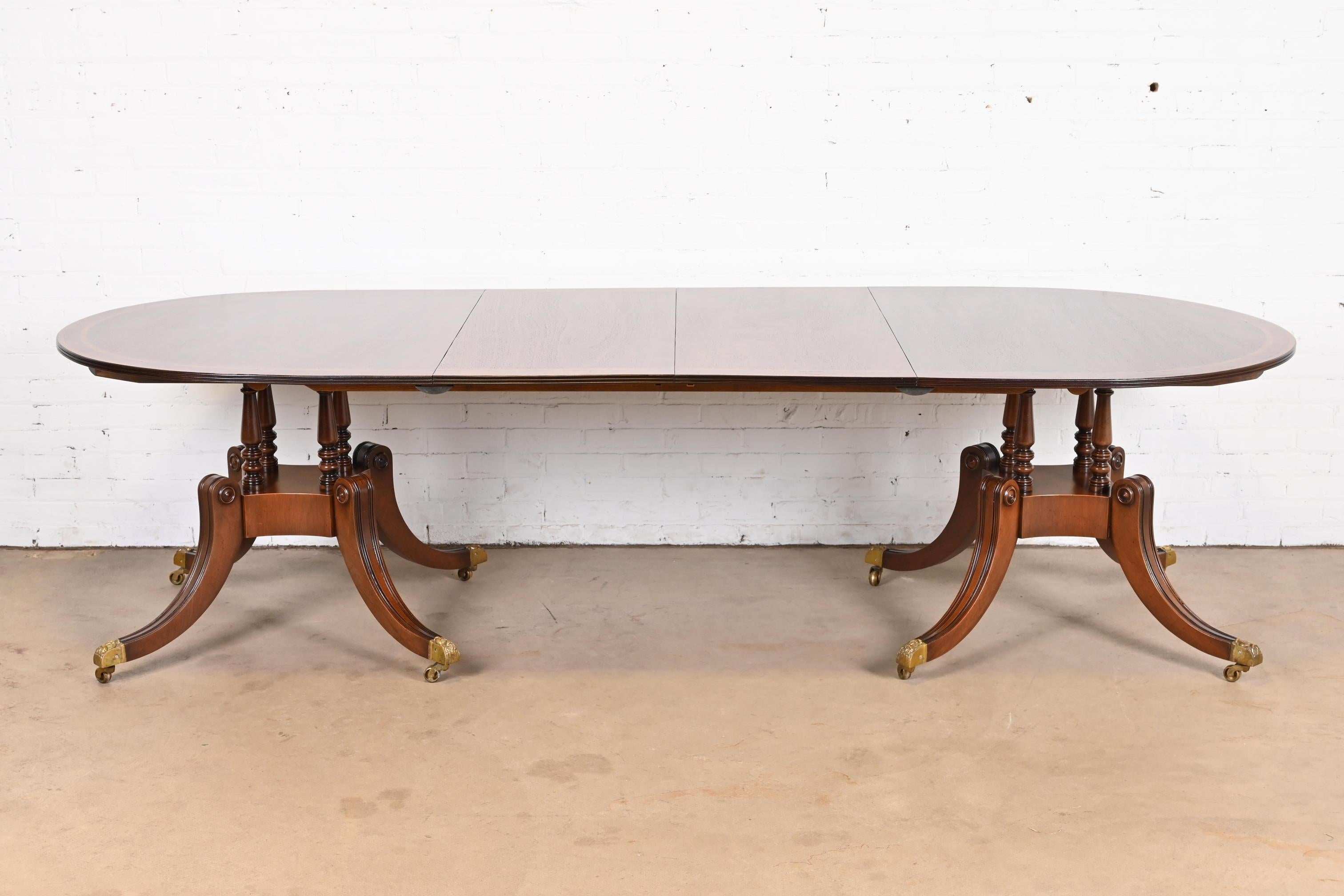 An exceptional Georgian or Regency style double pedestal extension dining table

In the manner of Baker Furniture

USA, Circa Mid-20th Century

Gorgeous mahogany, with satinwood and rosewood banding, carved solid mahogany pedestals, brass-capped paw