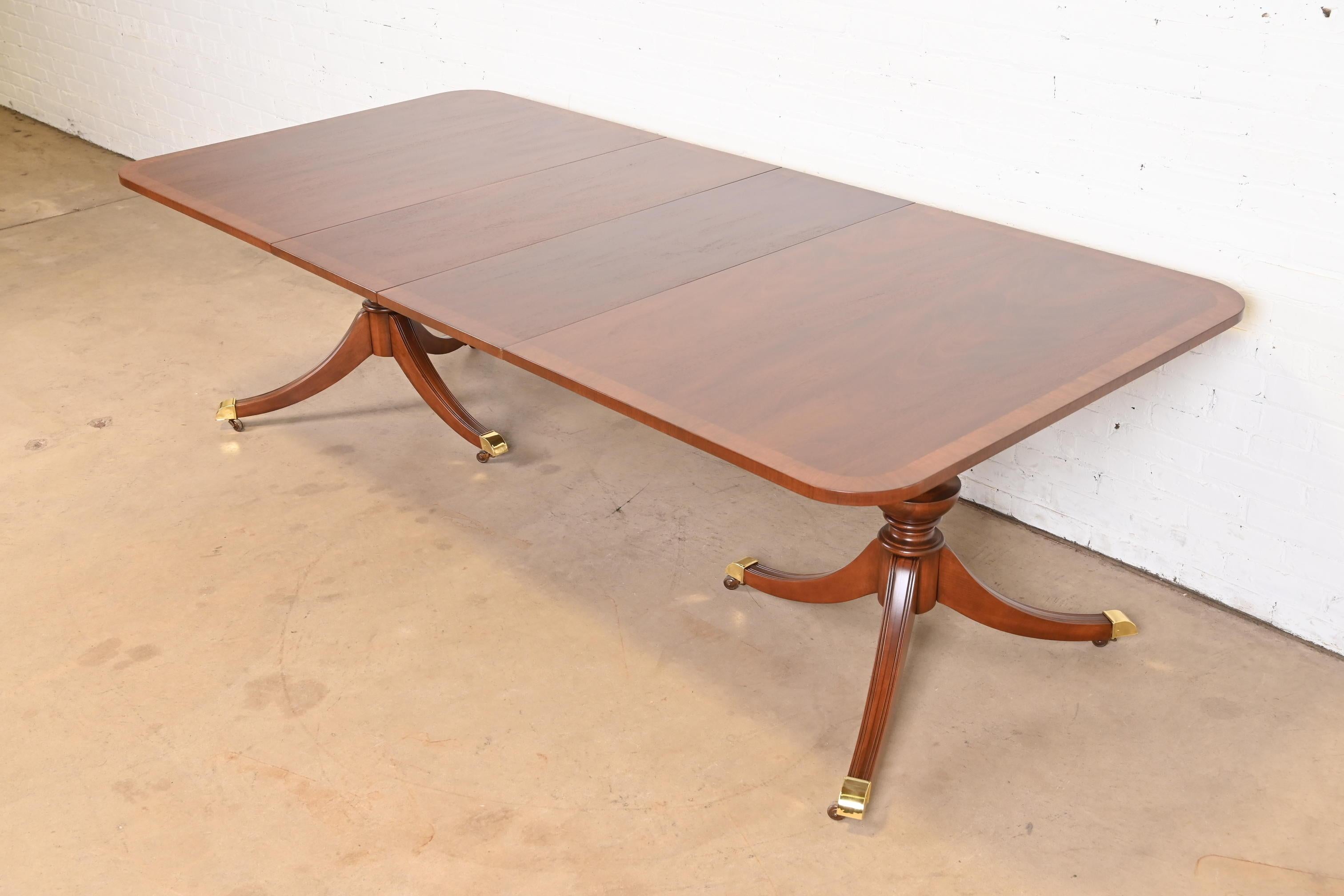 A gorgeous Georgian or Regency style double pedestal extension dining table

In the manner of Baker Furniture

USA, Late 20th Century

Beautiful book-matched banded mahogany, with carved solid mahogany pedestals, and brass-capped feet on brass