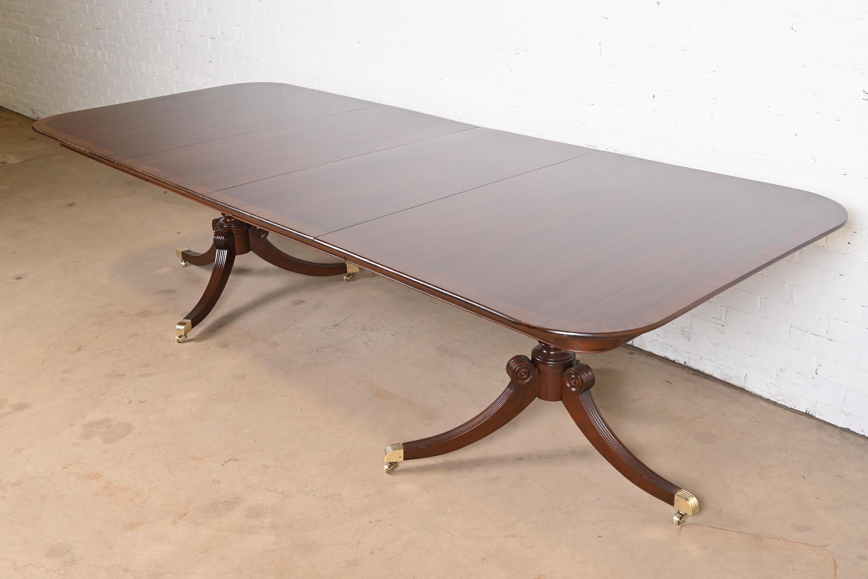 A gorgeous Georgian or Regency style double pedestal extension dining table

In the manner of Baker Furniture

USA, Circa 1980s

Beautiful banded mahogany, with carved solid mahogany pedestals, and brass-capped feet on brass casters.

Measures: 68