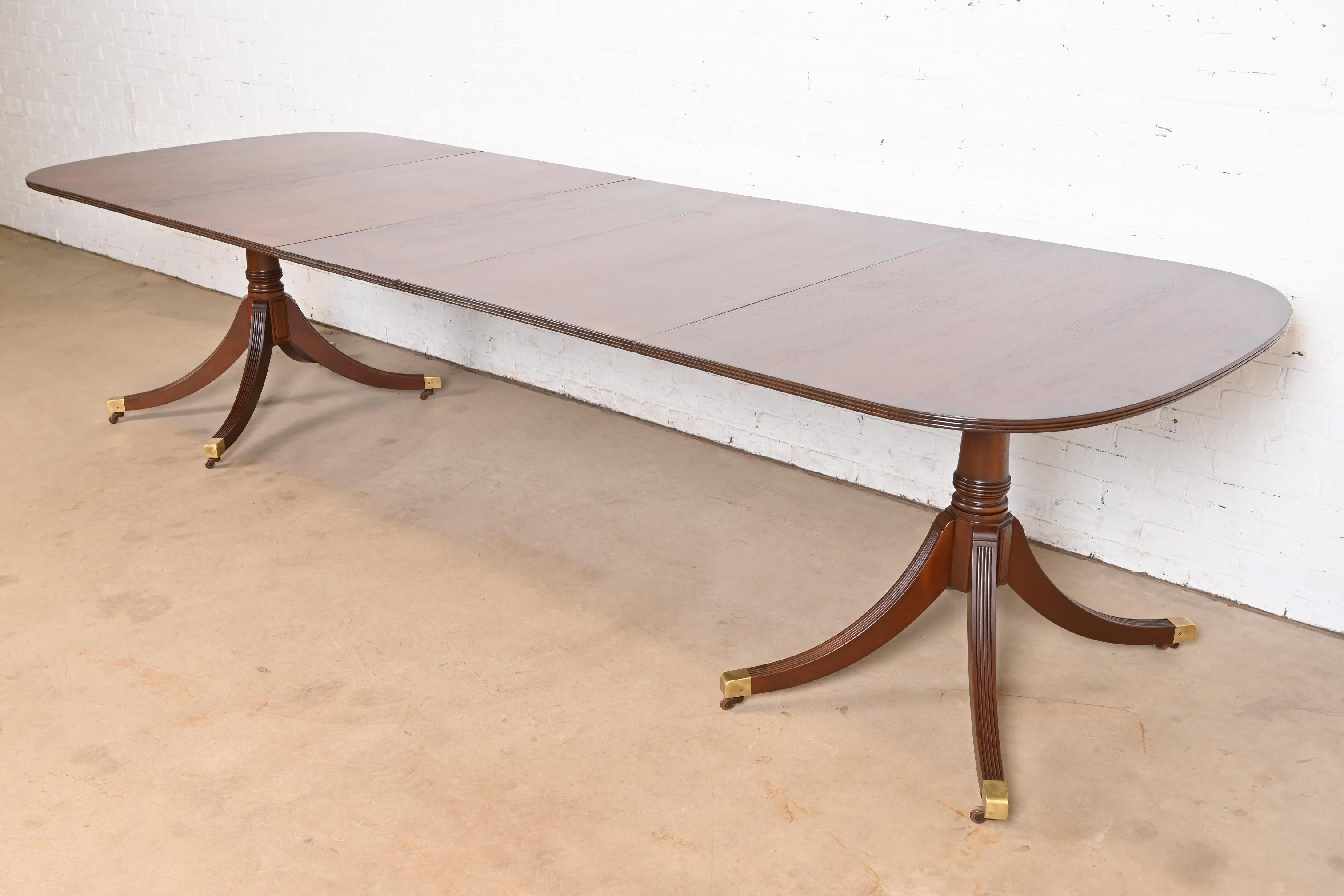 An exceptional Georgian or Regency style double pedestal extension dining table

In the manner of Baker Furniture

USA, Circa 1980s

Gorgeous mahogany top, with flame mahogany banding, carved solid mahogany pedestals, and brass-capped feet on