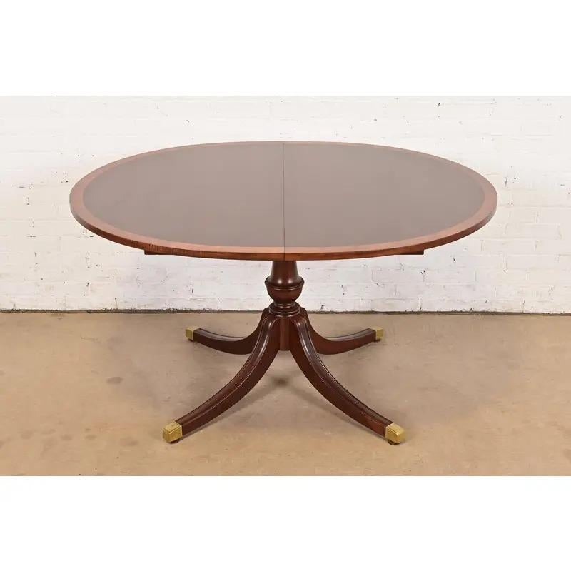 An exceptional Georgian or Regency style pedestal extension dining table

In the manner of Baker Furniture

USA, Circa 1980s

Beautiful mahogany top, with satinwood banding, carved solid mahogany pedestal, and brass capped feet.

Measures: 54
