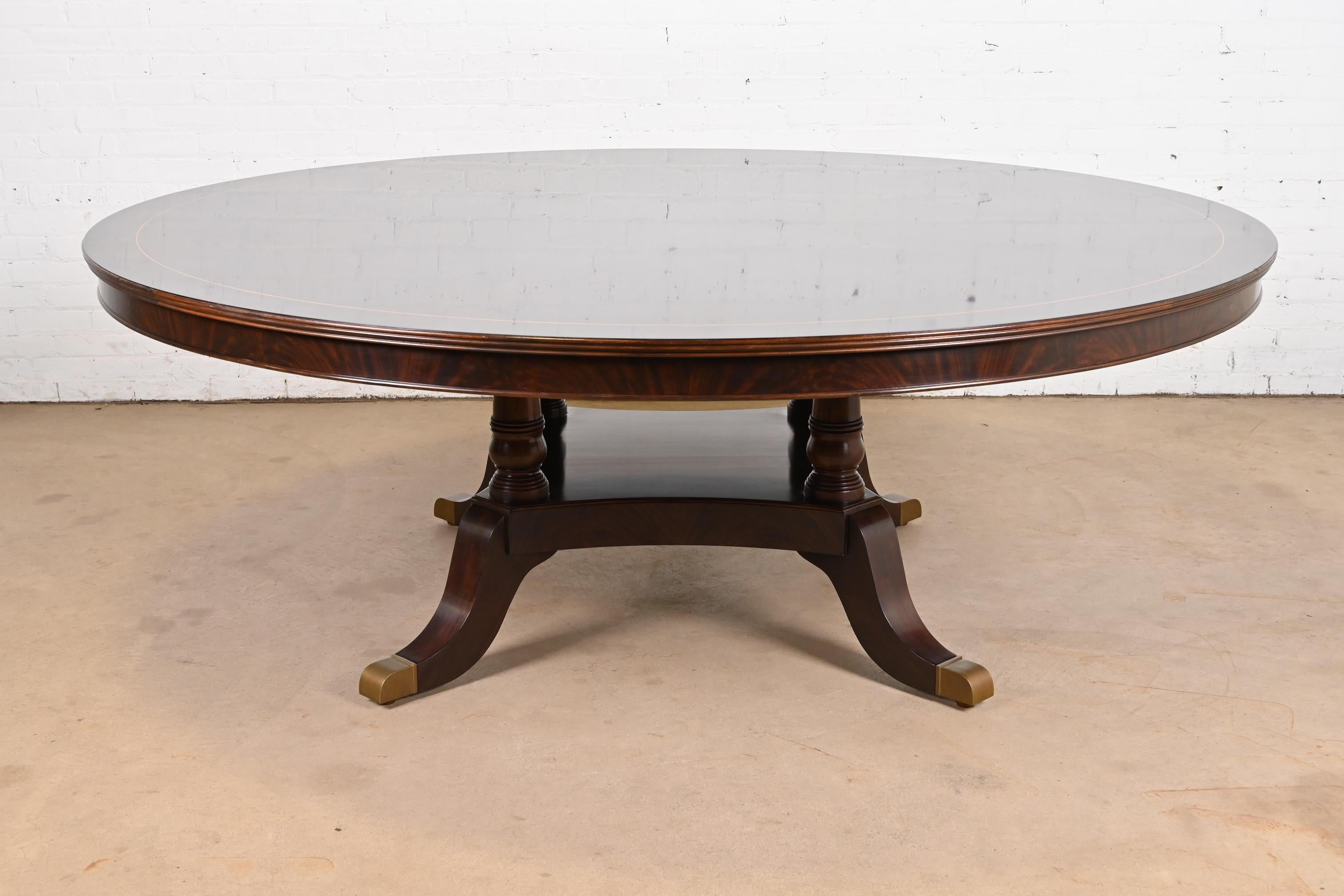 A beautiful Georgian or Regency style pedestal round dining table

In the manner of Baker Furniture

USA, Circa Late 20th Century

Gorgeous starburst book-matched flame mahogany top, with satinwood string inlay banding, and carved solid mahogany