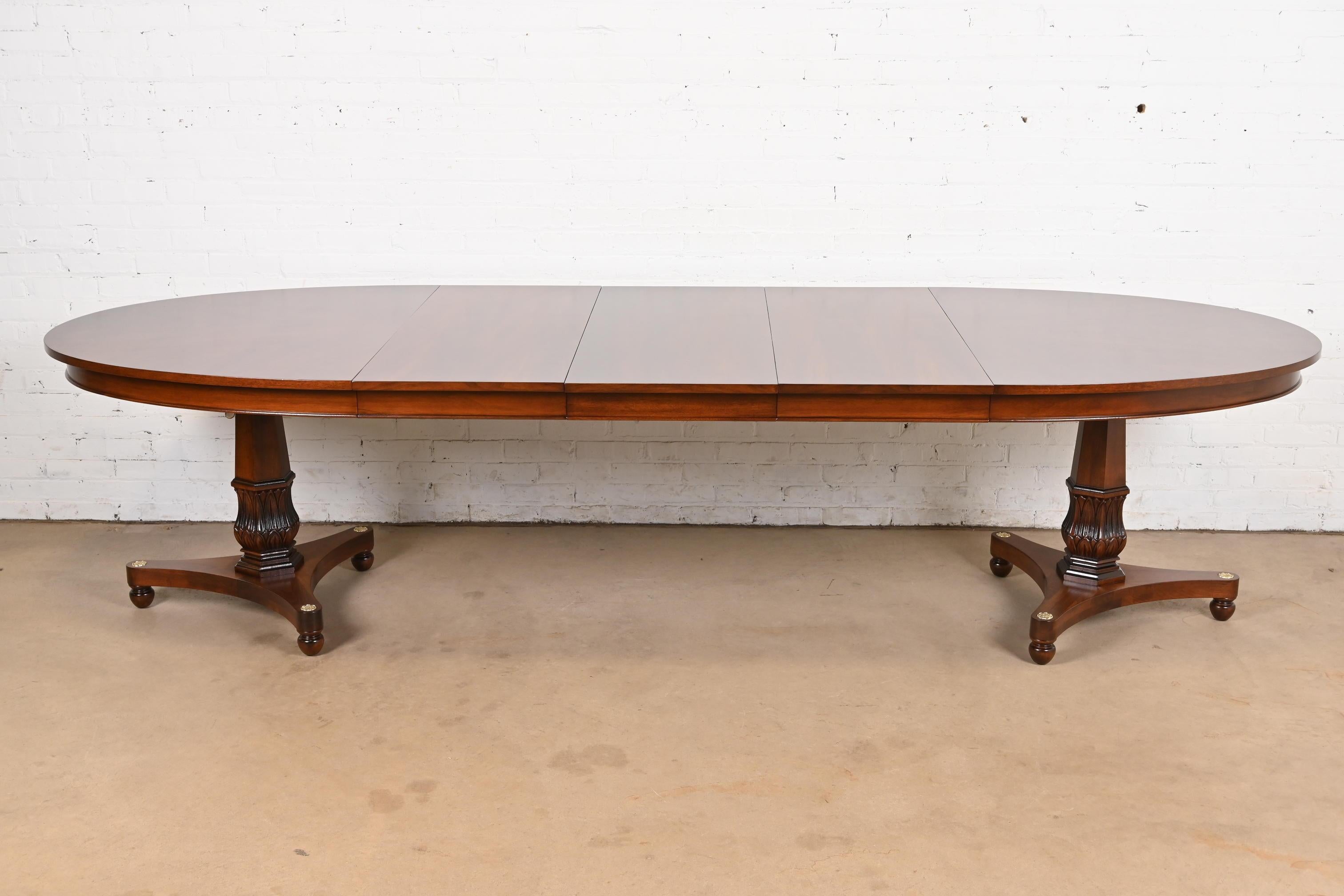 An outstanding Regency or Neoclassical style double pedestal extension dining table

In the manner of Baker Furniture

USA, Circa 1960s

Gorgeous book-matched walnut top in starburst pattern, with carved walnut pedestals and brass
