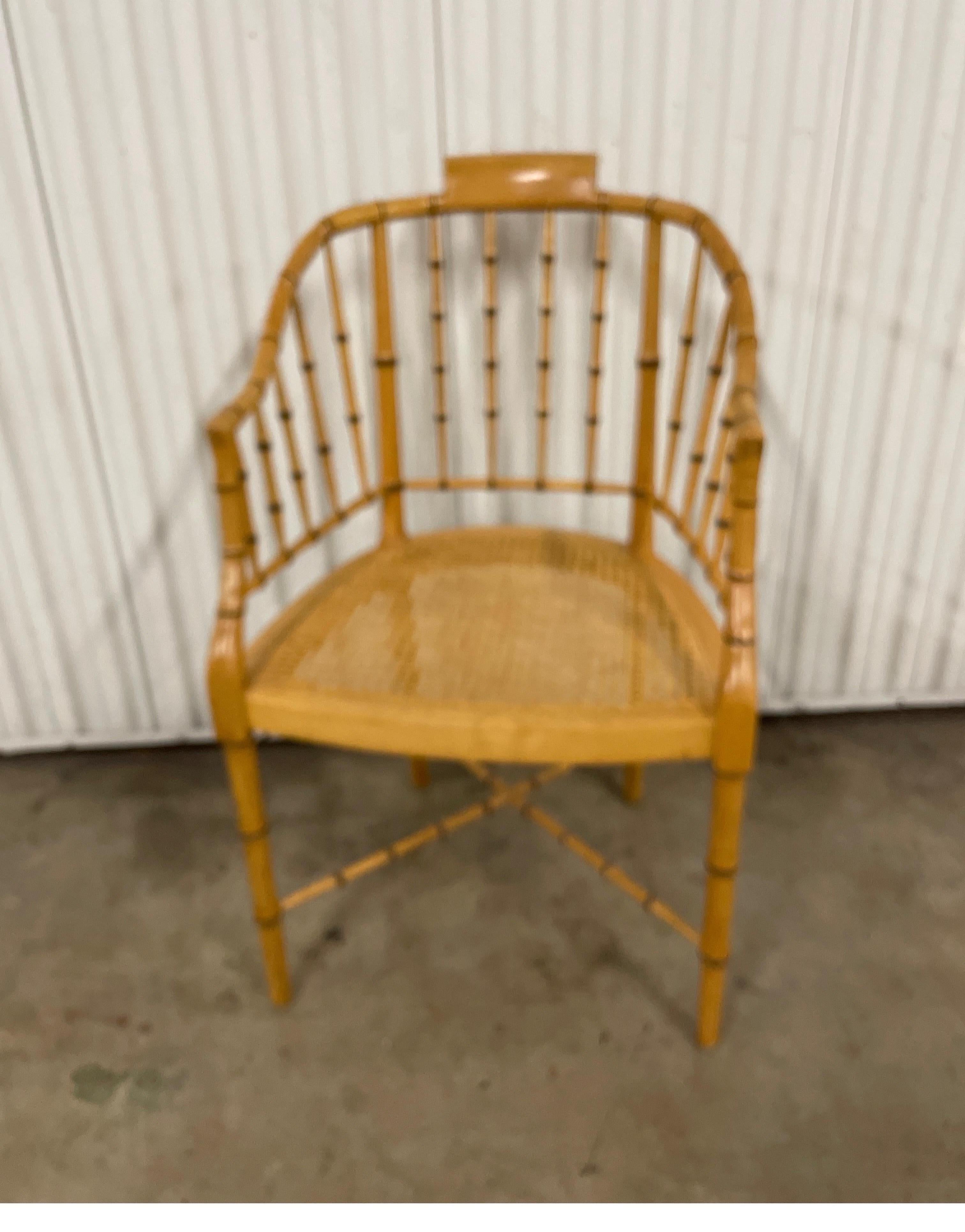 Vintage faux bamboo tub style armchair with cane seat. This circa 1960 armchair made by Baker furniture features a tub shaped back with curved arms & a cane seat. Legs are connected by an X form cross stretcher. This elegant blond finish chair will