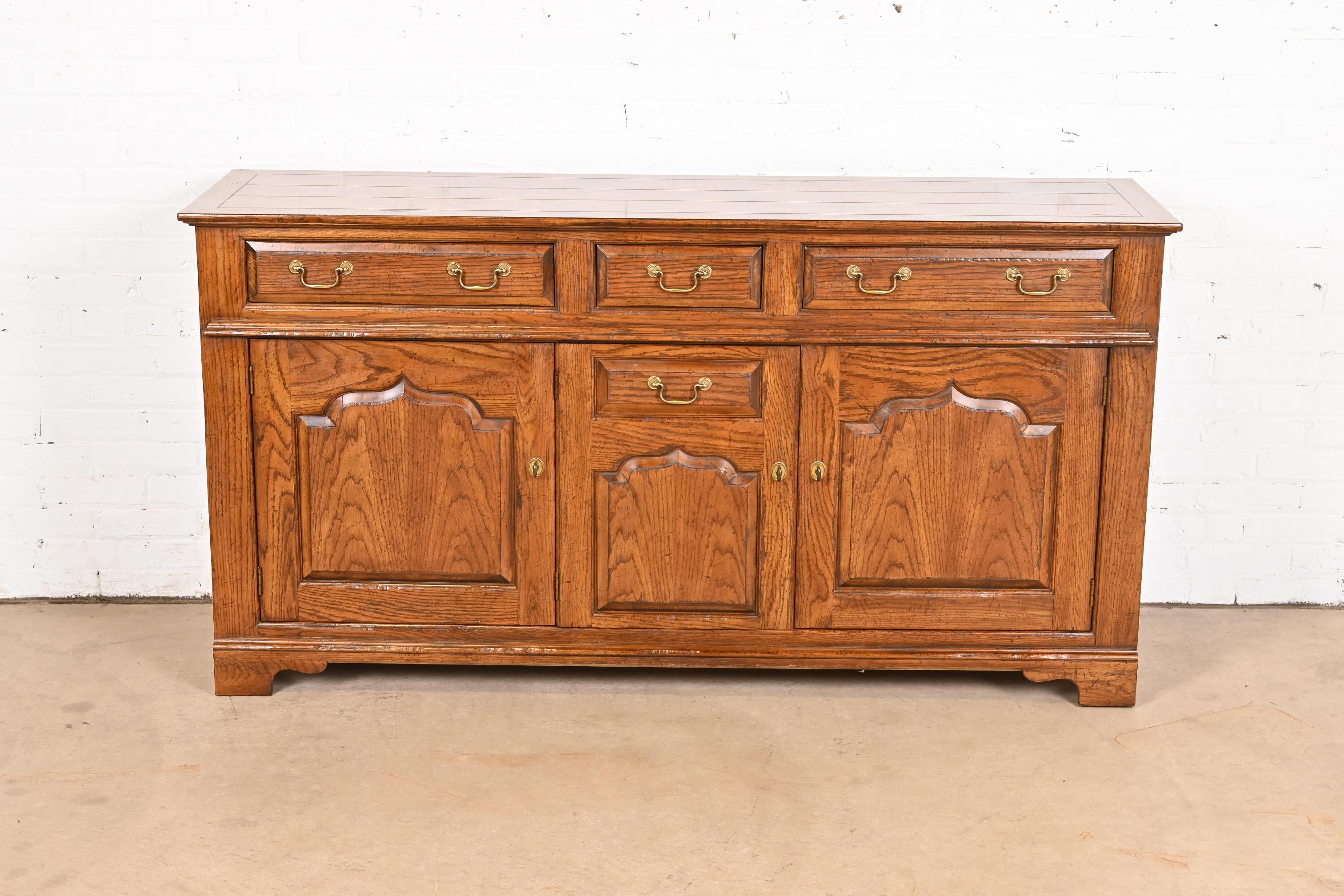 A beautiful Welsh, English Traditional, or Georgian sideboard, buffet server, or bar cabinet

By Baker Furniture

USA, Circa 1970s

Carved oak, with original brass hardware.

Measures: 68