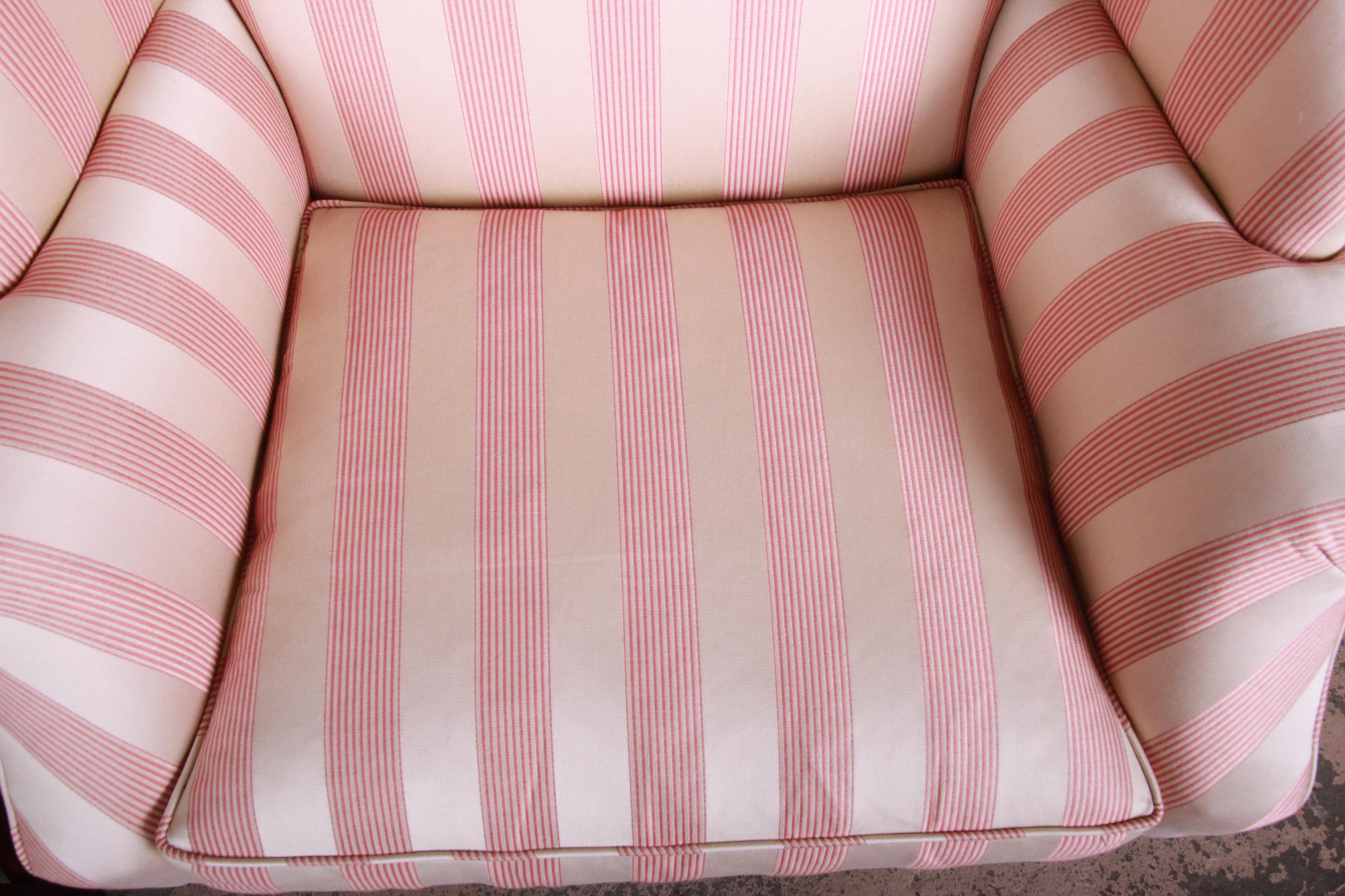 A gorgeous wingback lounge chair by Baker Furniture. The chair features solid mahogany tapered legs, scrolled arms, and beautiful original upholstery in cream with pink stripes. A very comfortable and elegant chair. It is made with the highest
