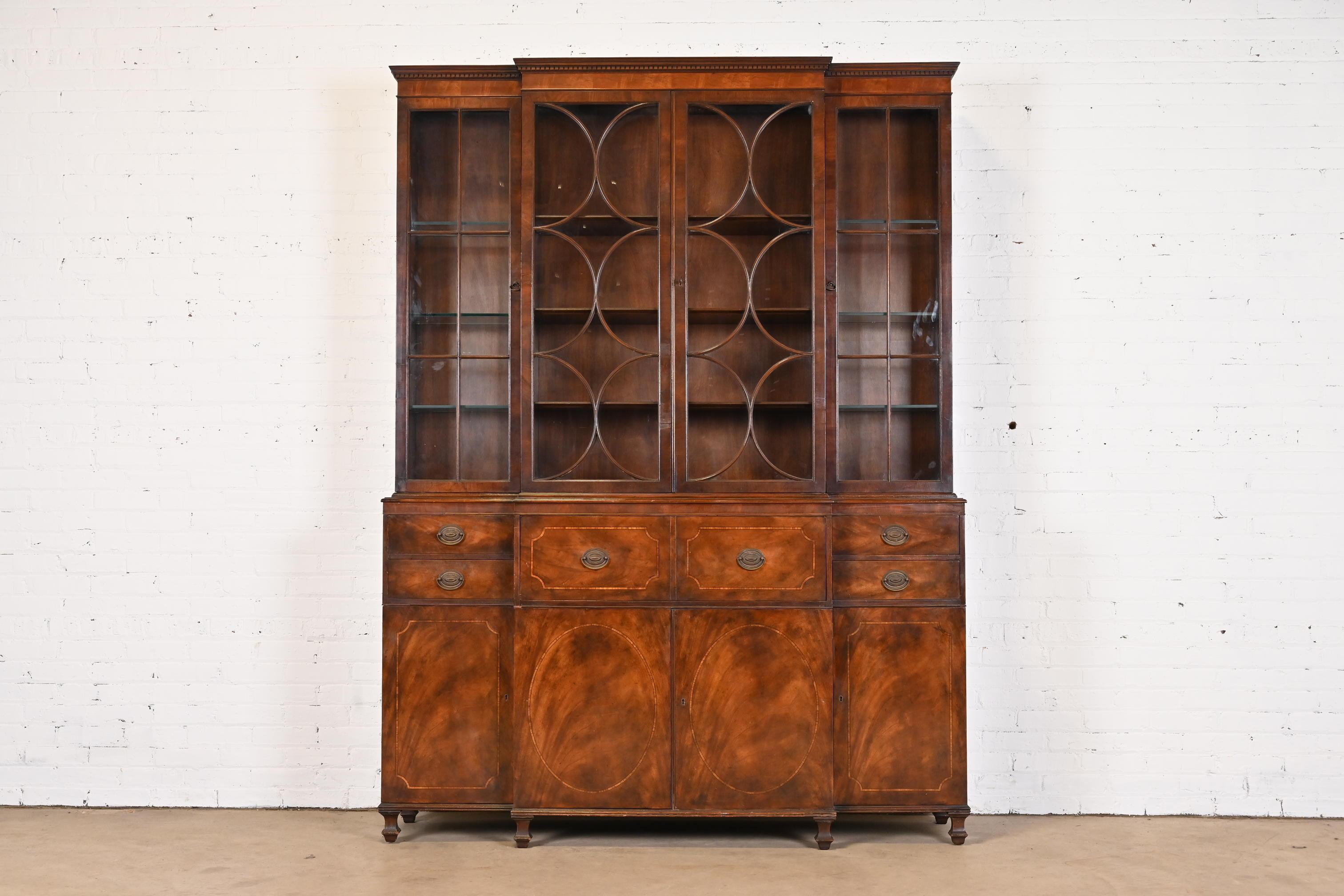 A gorgeous English Georgian style two-piece breakfront bookcase cabinet with drop-front secretary desk

By Baker Furniture

USA, Circa 1940s

Book-matched flame mahogany with satinwood inlay, mullioned glass front doors, original brass