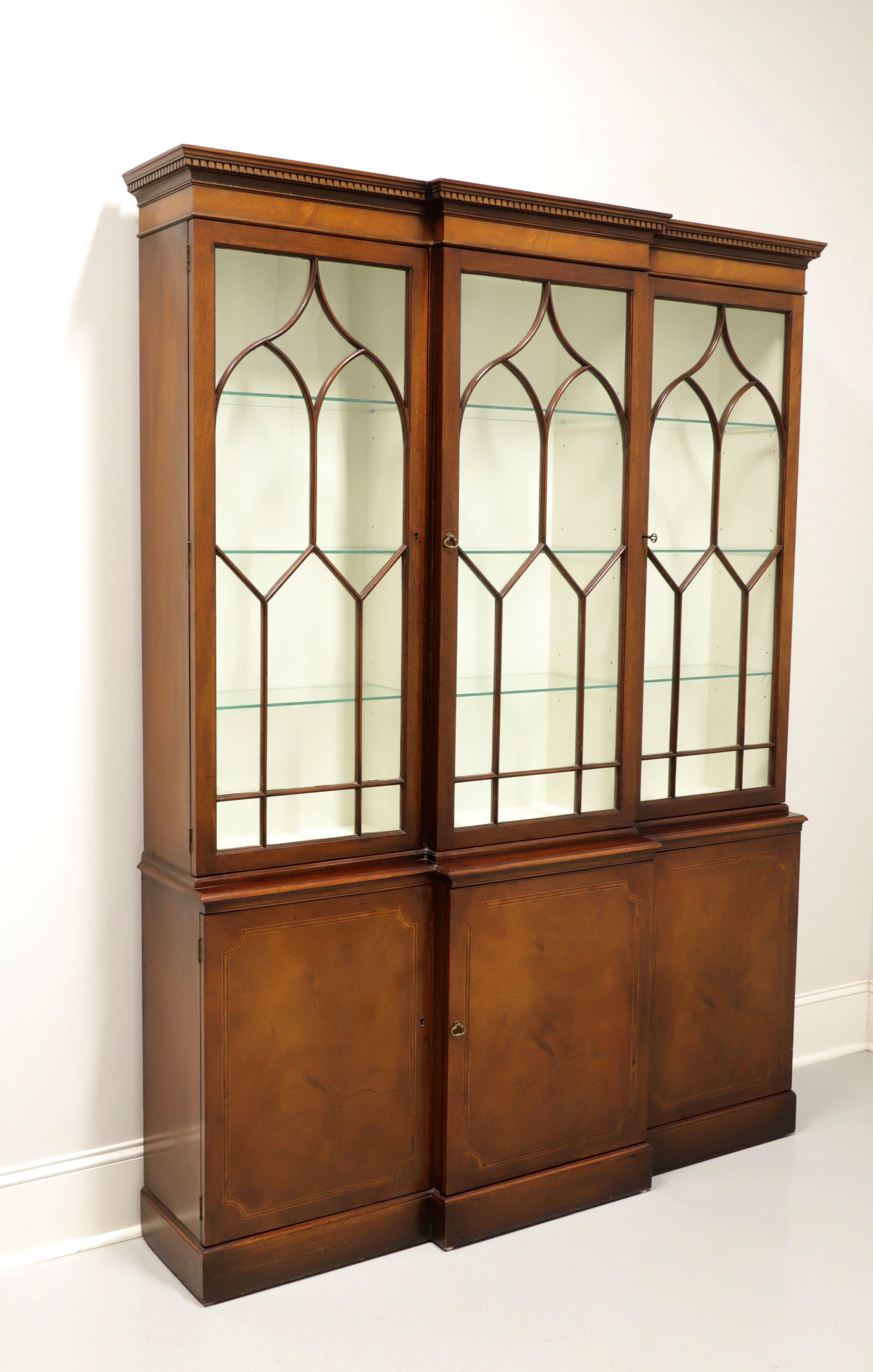 A Georgian style breakfront china cabinet by Baker Furniture. Mahogany with brass hardware, fretwork to glass doors, banded door fronts and crown & dentil molding to the top. Upper lighted cabinet features three compartments with three adjustable