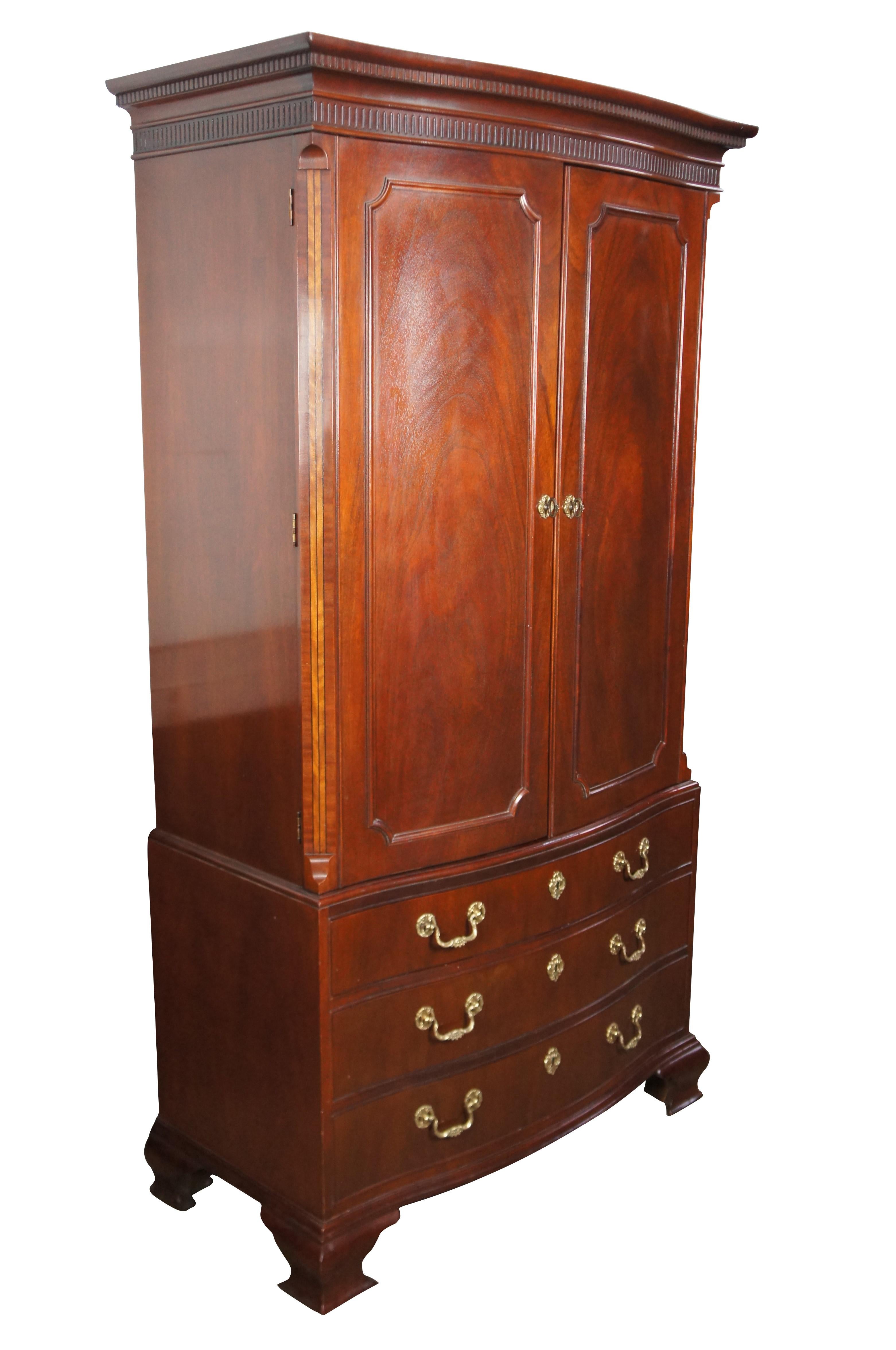 1980s Baker Furniture Georgian Style Armoire or Wardrobe.  Made from mahogany with a serpentine bowfront and chamfered stiles with striped inlay terminating into a rams tongue. The cabinet opens to a linen press format with shelves for clothing over