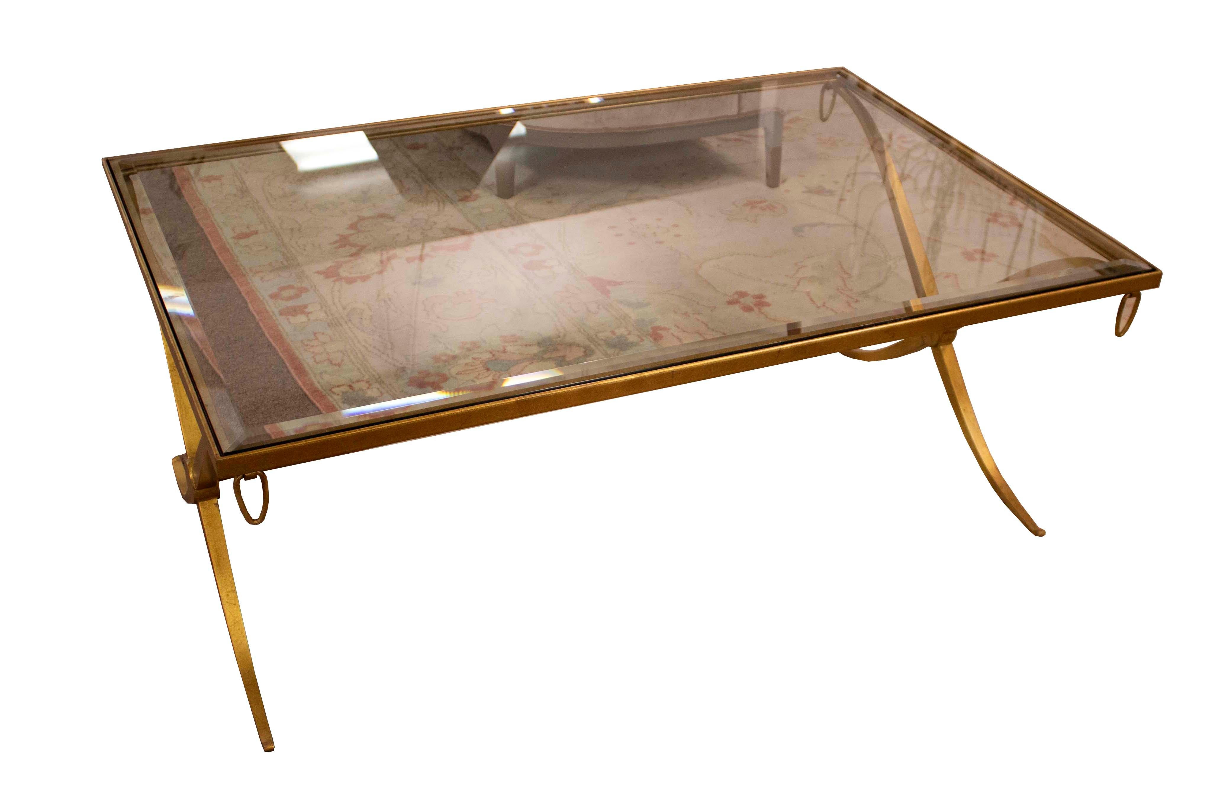 Up for offer is this sophisticated cocktail table with a beveled glass top and accented by a gold leaf metal x-base. Clean lines make this piece versatile enough for most aesthetics.
 