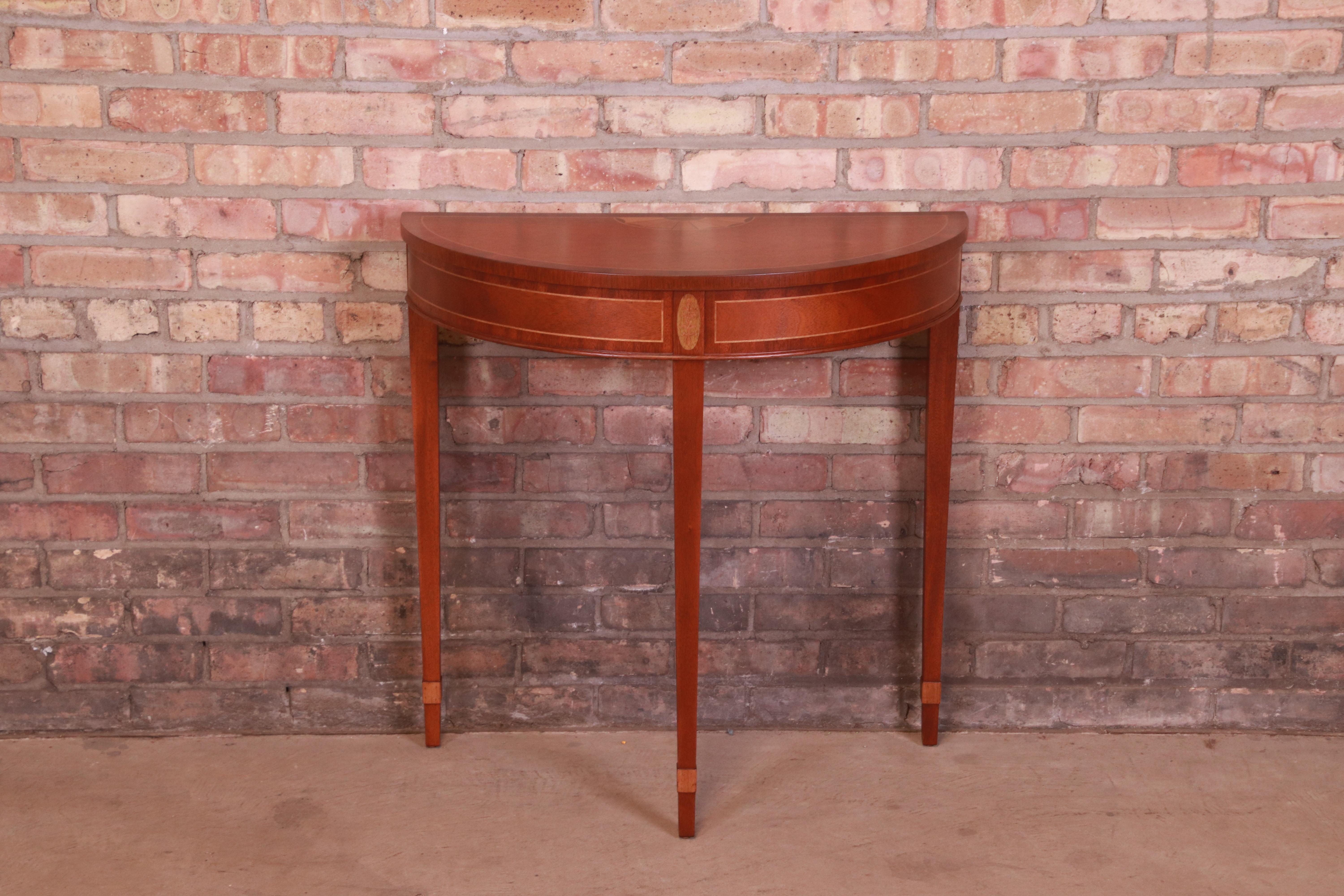 An exceptional petite Hepplewhite or Federal style demilune console table or entry table

By Baker Furniture

USA, Circa 1980s

Mahogany, with satinwood string inlay and marquetry.

Measures: 29
