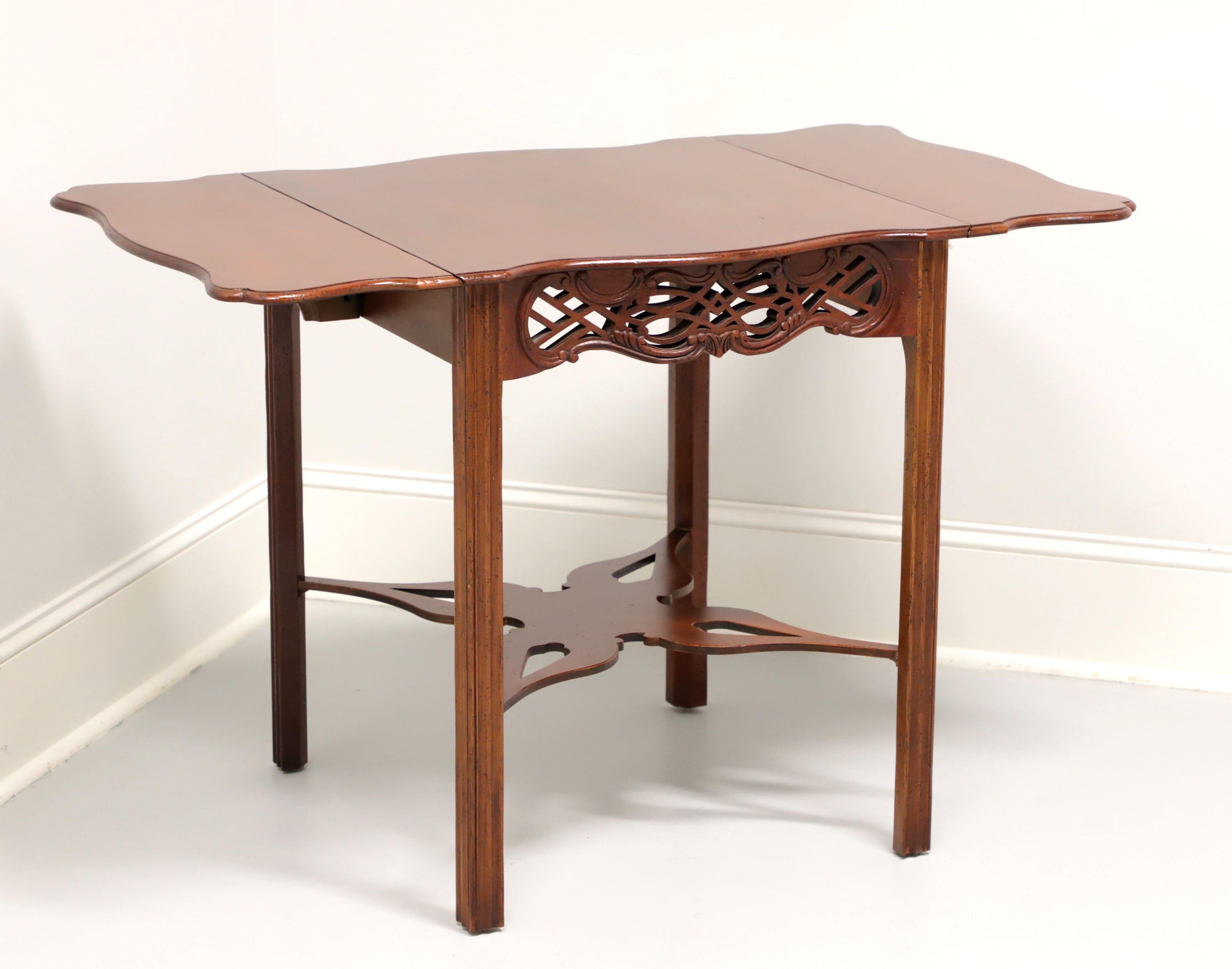 A Georgian style Pembroke table by Baker Furniture, from their Historic Charleston Reproductions Collection. Solid mahogany with a distressed finish, drop leaves, ornately carved apron, butterfly shaped open carved under tier, and fluted straight