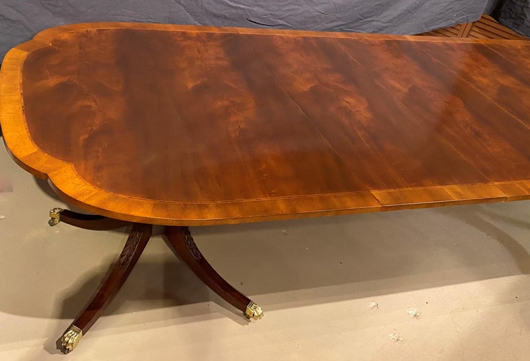 A fine Regency style mahogany double pedestal dining table with three finished leaves, made by Baker Furniture for the Historic Charleston Collection, with shaped banded and inlaid top, and two foliate carved pedestals with four downswept legs,