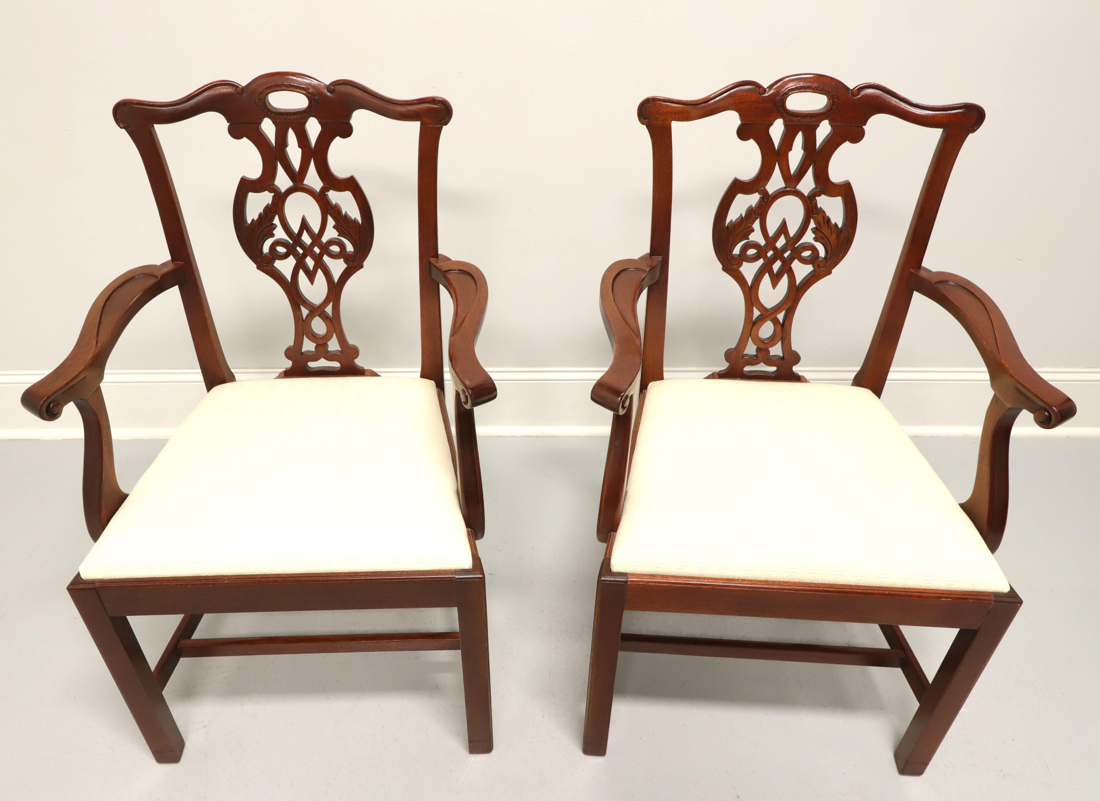 A pair of dining armchairs in the Chippendale style by Baker Furniture, from their Historic Charleston Collection. Solid mahogany with a lighter finish, carved crest rail, carved seat back, curved arms, neutral cream color fabric upholstered seat,