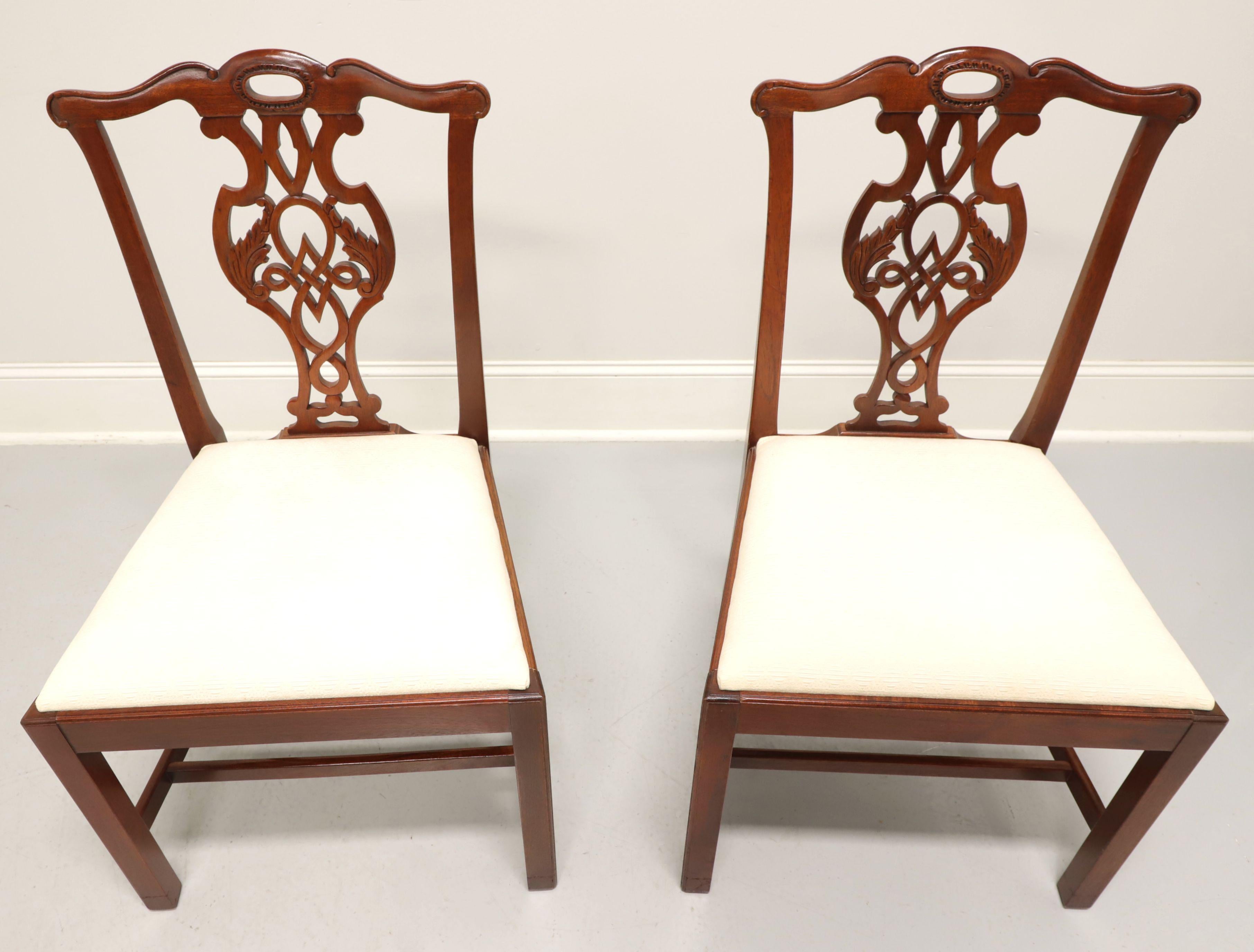 A pair of dining side chairs in the Chippendale style by Baker Furniture, from their Historic Charleston Collection. Solid mahogany with a lighter finish, carved crest rail, carved seat back, neutral cream color fabric upholstered seat, straight