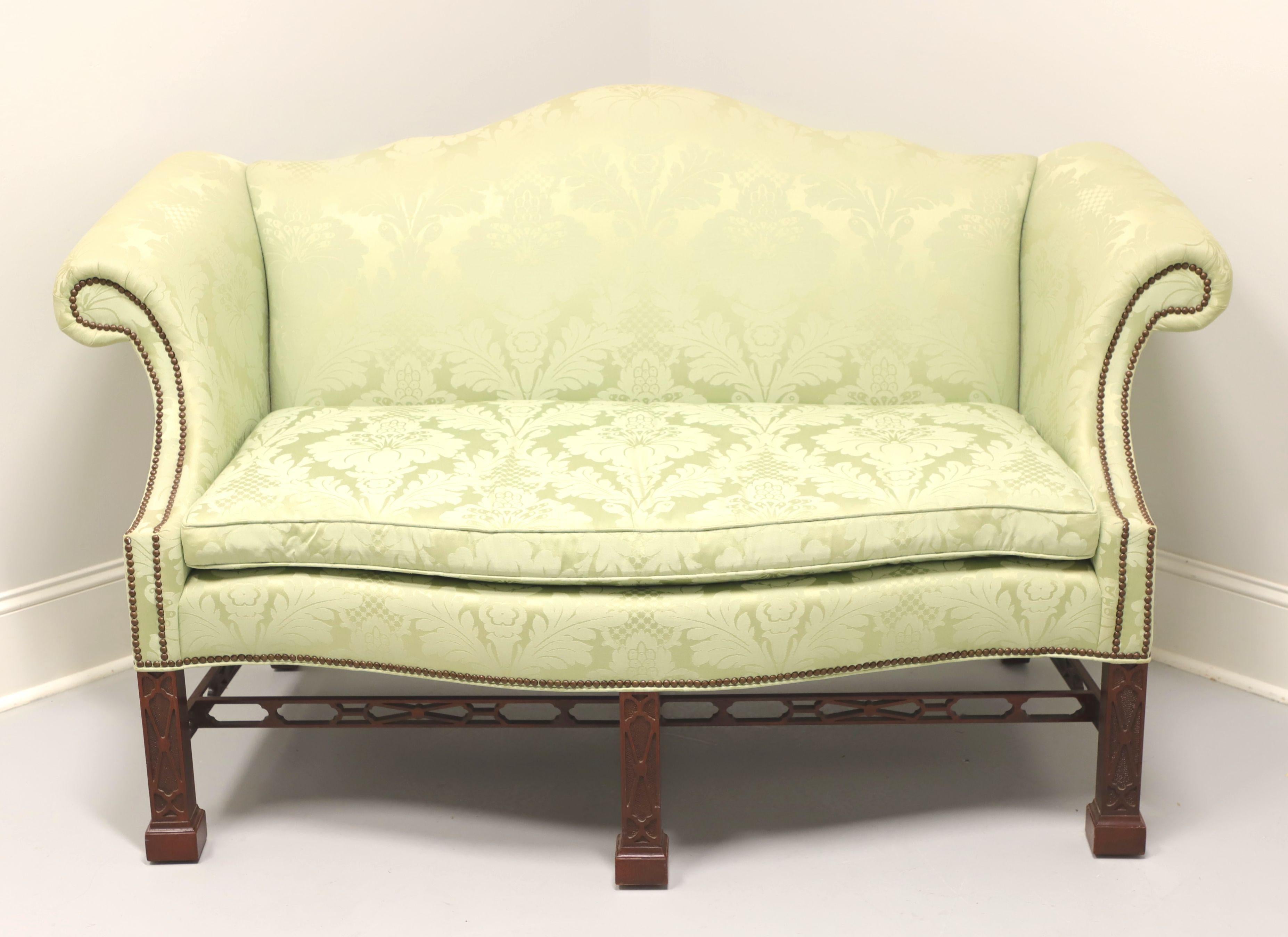 A Chippendale style camel back settee by Baker Furniture, from their Historic Charleston Reproductions Collection. Mahogany frame, camel back, rolled arms, brass nail head trim, single reversible seat cushion, fretwork stretchers, three saber back