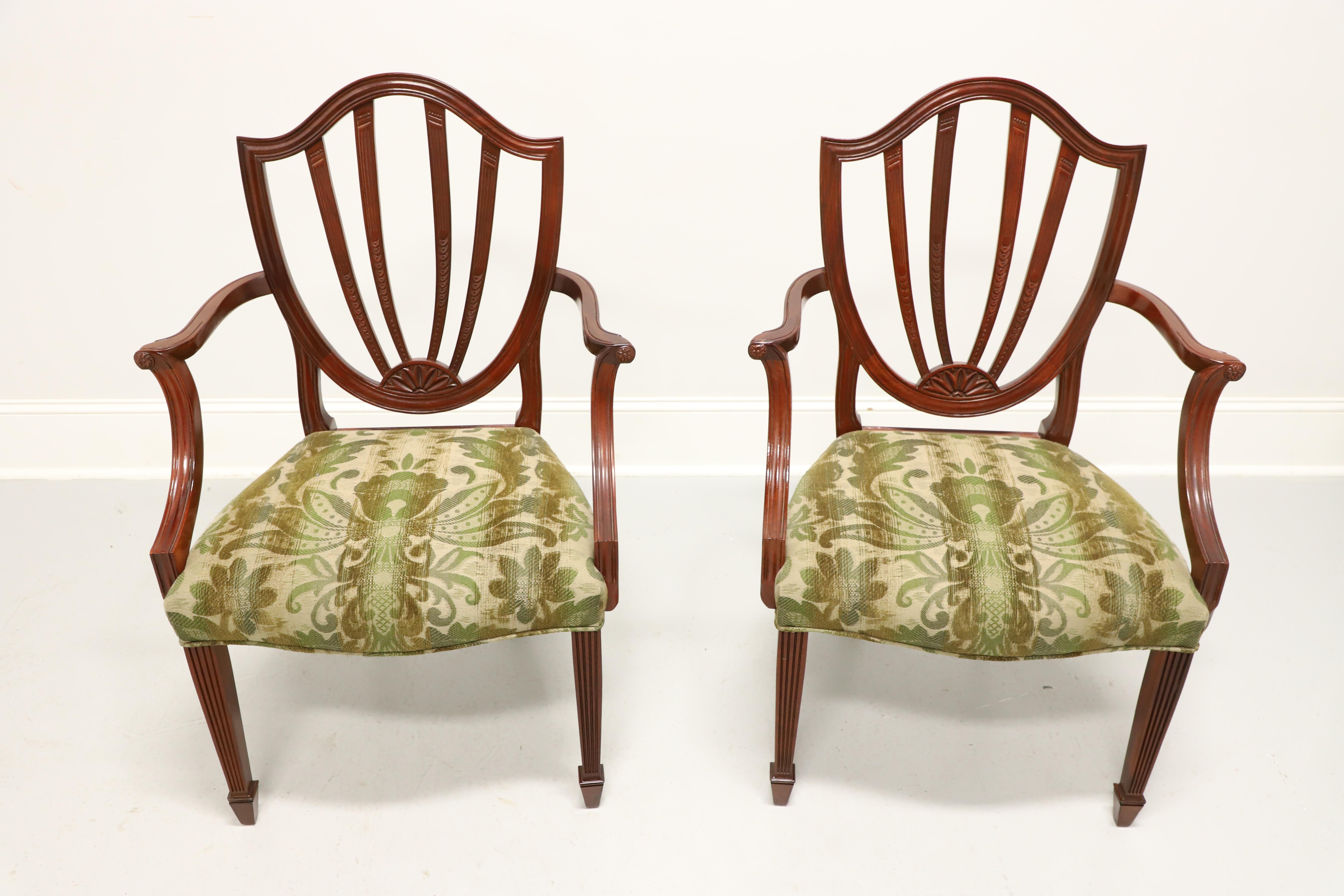 A pair of dining armchairs in the Georgian Hepplewhite style by Baker Furniture, from their Historic Charleston Reproductions Collection. Solid mahogany with carved shield backs, gently curved arms with fluted carved supports, green & beige color