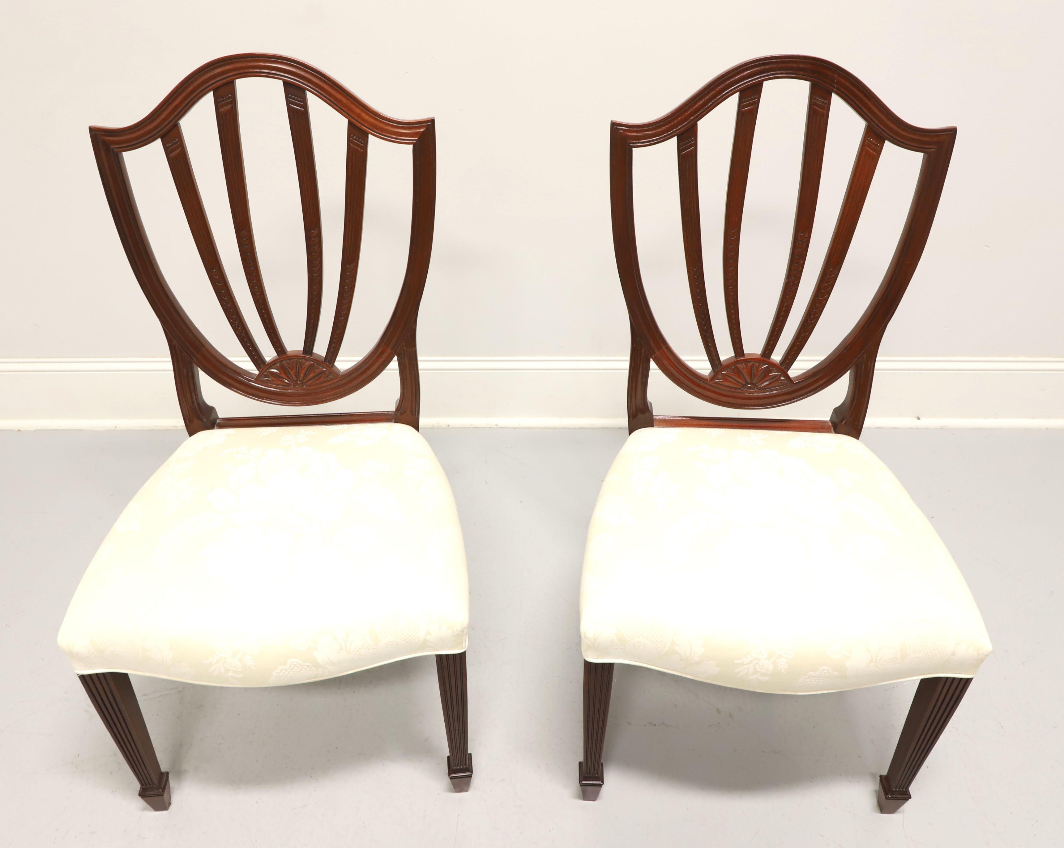 A pair of dining side chairs in the Georgian Hepplewhite style by Baker Furniture, from their Historic Charleston Reproductions Collection. Solid mahogany, carved open shield backrests with a leaf motif, cream colored brocade fabric upholstered
