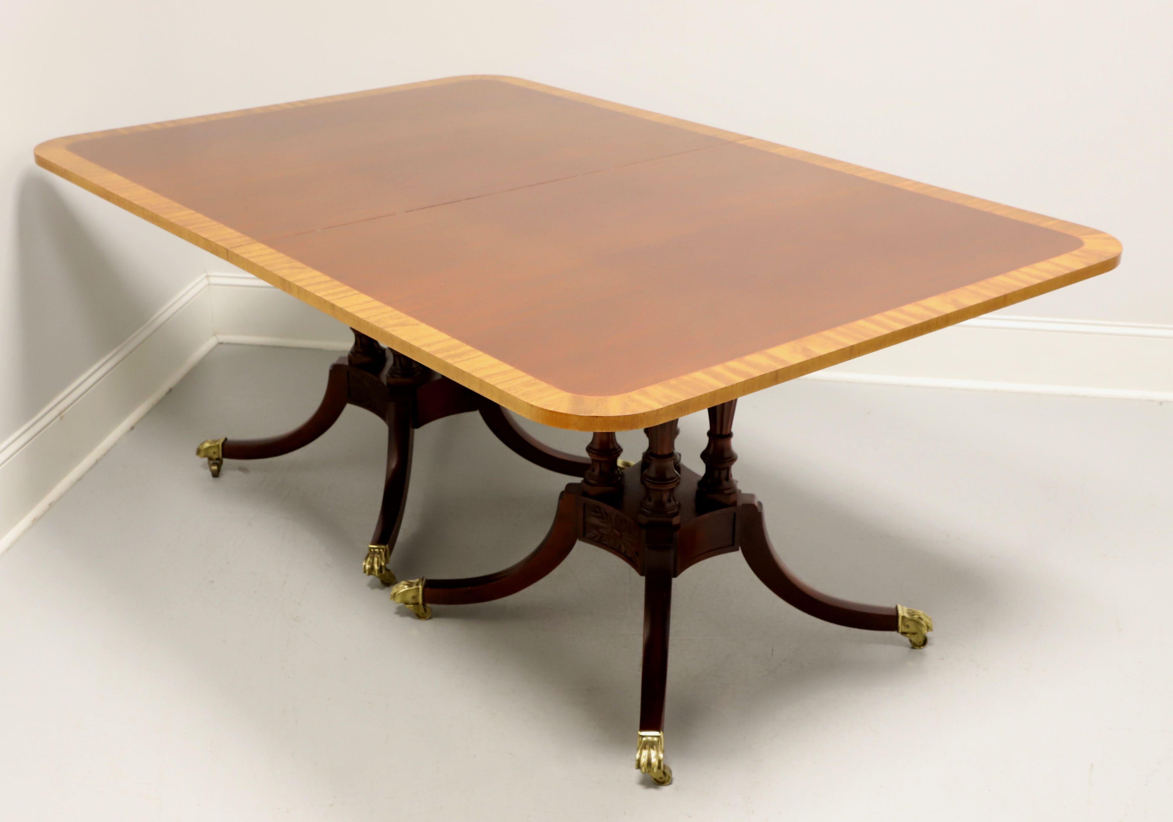 A Regency style double pedestal dining table by Baker Furniture, from their Historic Charleston Reproductions Collection. Mahogany with satinwood banding to top & edge, decoratively carved birdcage double pedestals with four legs, brass paw toe caps