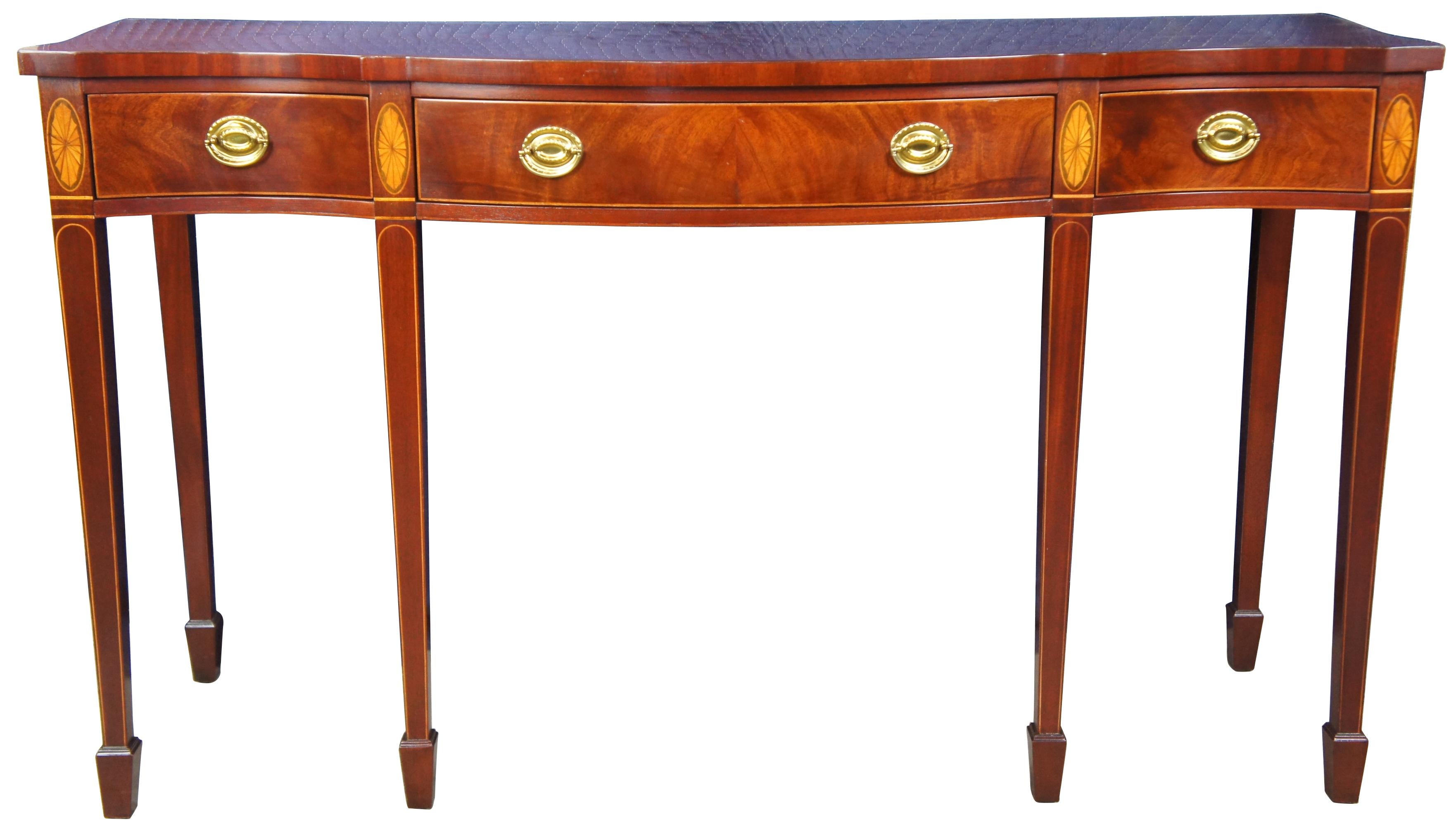 Baker Historic Charleston three-drawer mahogany console table, circa 1990s. Features a mixture of Federal and Sheraton styling with a serpentine front leading to bookmatched mahogany with satinwood inlay, brass hardware, and long tapered legs