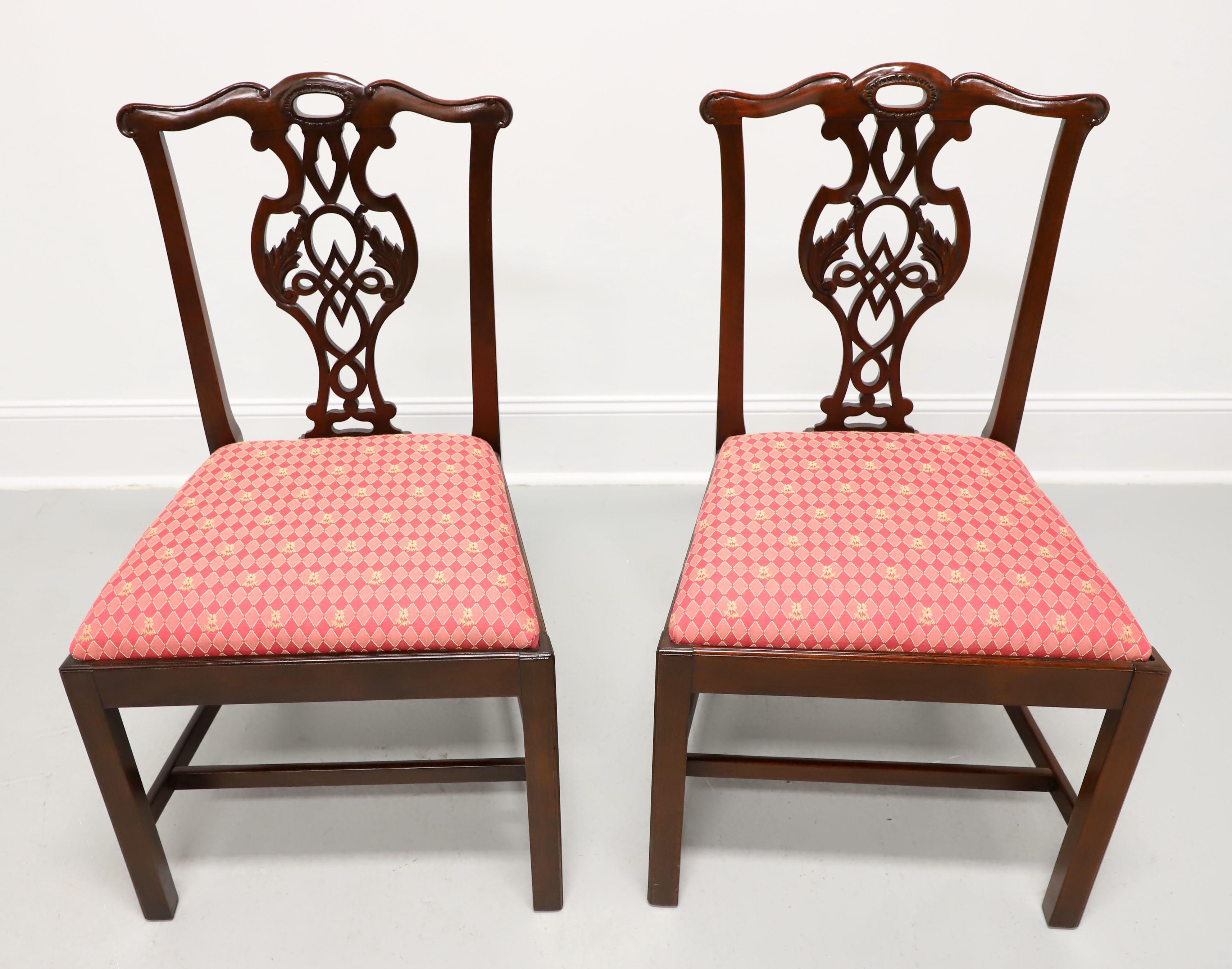A pair of dining side chairs in the Chippendale style by Baker Furniture, from their Historic Charleston Collection. Solid mahogany with a carved crest rail, carved seat back, shades of pink diamond pattern fabric upholstered seat, straight legs,