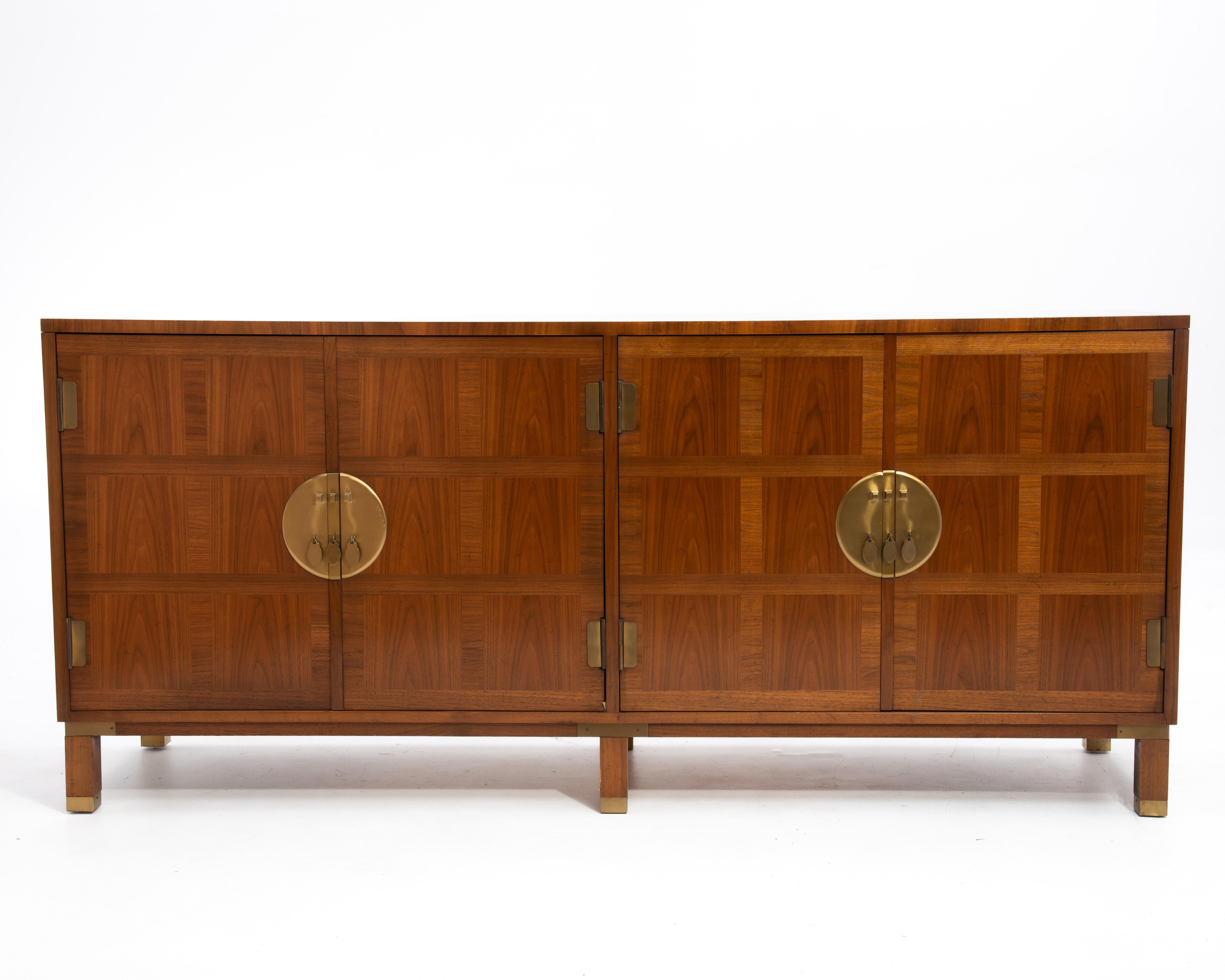 An unmarked Baker Milling Road credenza or sideboard from the early 1970s. Beautiful inlaid, banded walnut with brass hardware and feet. After the designs of Michael Taylor and Frank Van Steenberg for the Baker Far East Collection. 
When looking at