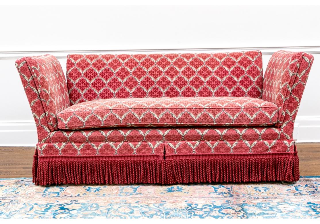 Feines Baker-Sofa im Knole-Stil mit klassischer (fester) Fallarmform, mit rechteckiger Rückenlehne und hohen Armen, die einen losen Kissensitz über einem Quastenrock flankieren. Gepolstert mit einem prächtigen roten Stoff mit weißen Federgittern,