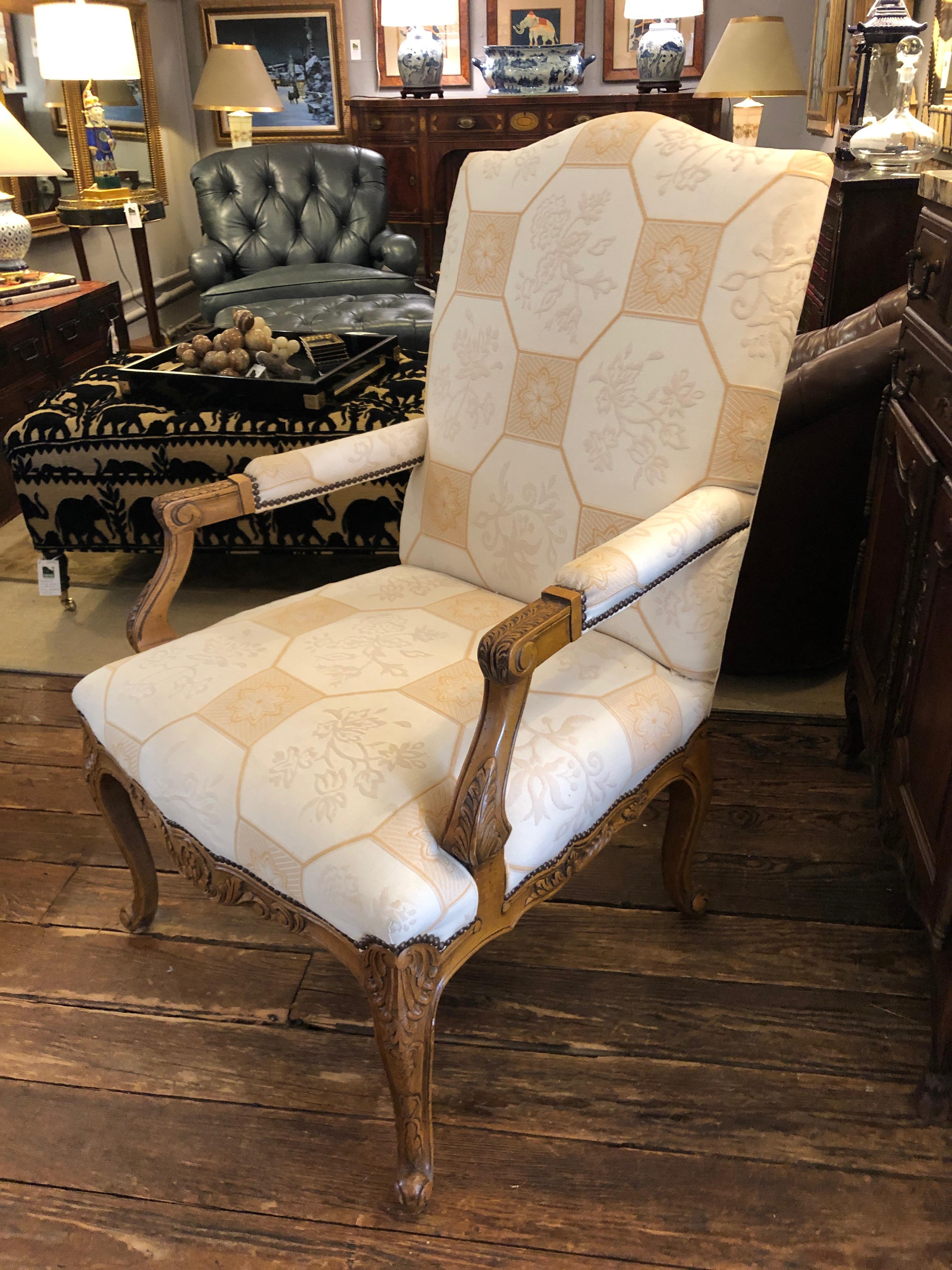 A beautiful roomy carved wood armchair having light color wood, cabriole legs, and neutral beige and tan geometric upholstery.