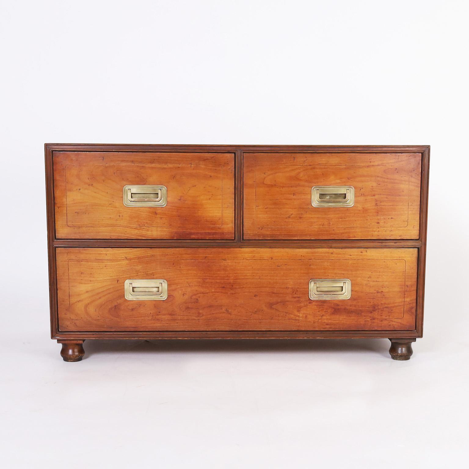 Chic vintage campaign style chest crafted in walnut with three drawers in a hip low form with brass hardware and turned feet. Signed in a drawer with a Baker silver label.