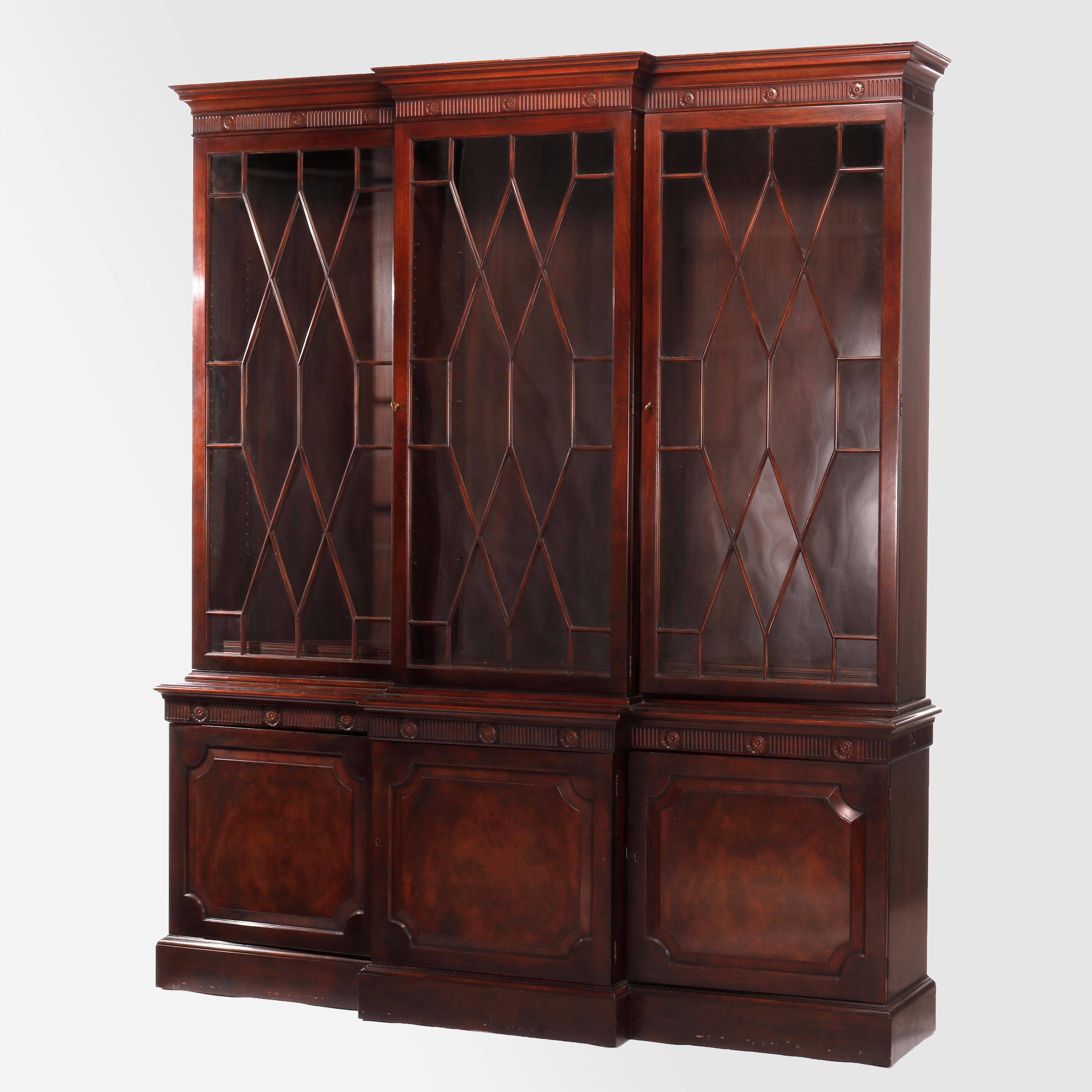 A step-back breakfront cupboard by Baker Furniture offers flame mahogany construction with triple mullioned glass doors opening to adjustable shelf and divided interior over lower cabinet with blind doors having flame mahogany reserves, reeded trim