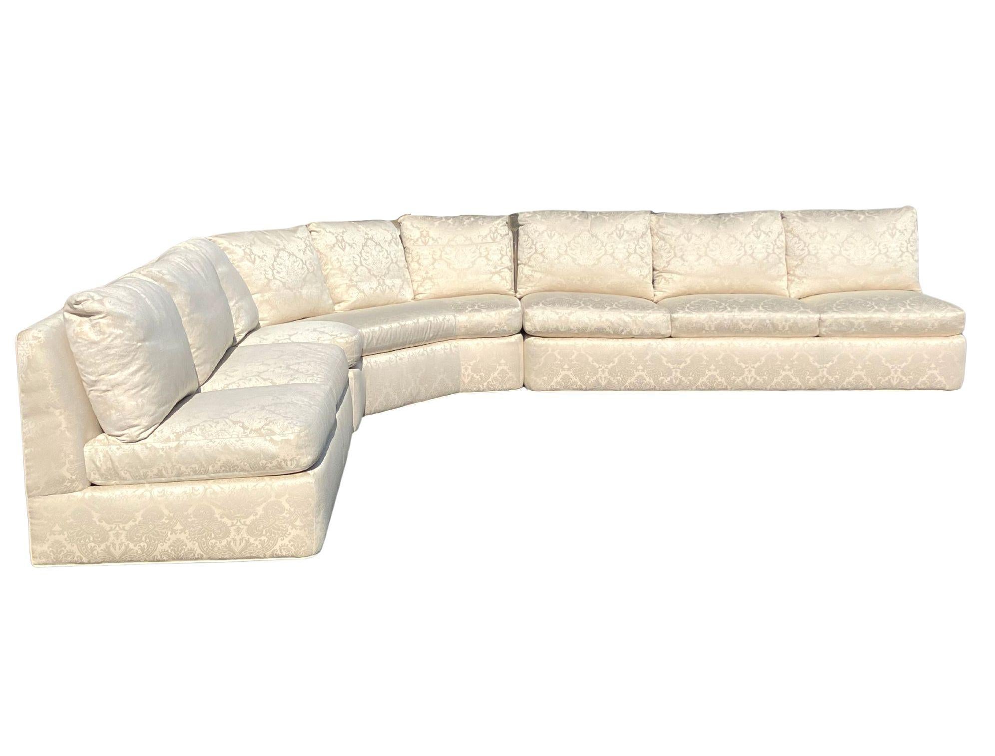 A Contemporary style three-piece sectional armless slipper sofa by Baker Furniture. Hardwood frame construction; upholstered in a soft white color brocade fabric, armless with a slipper style back, six reversible bottom cushions, nine reversible