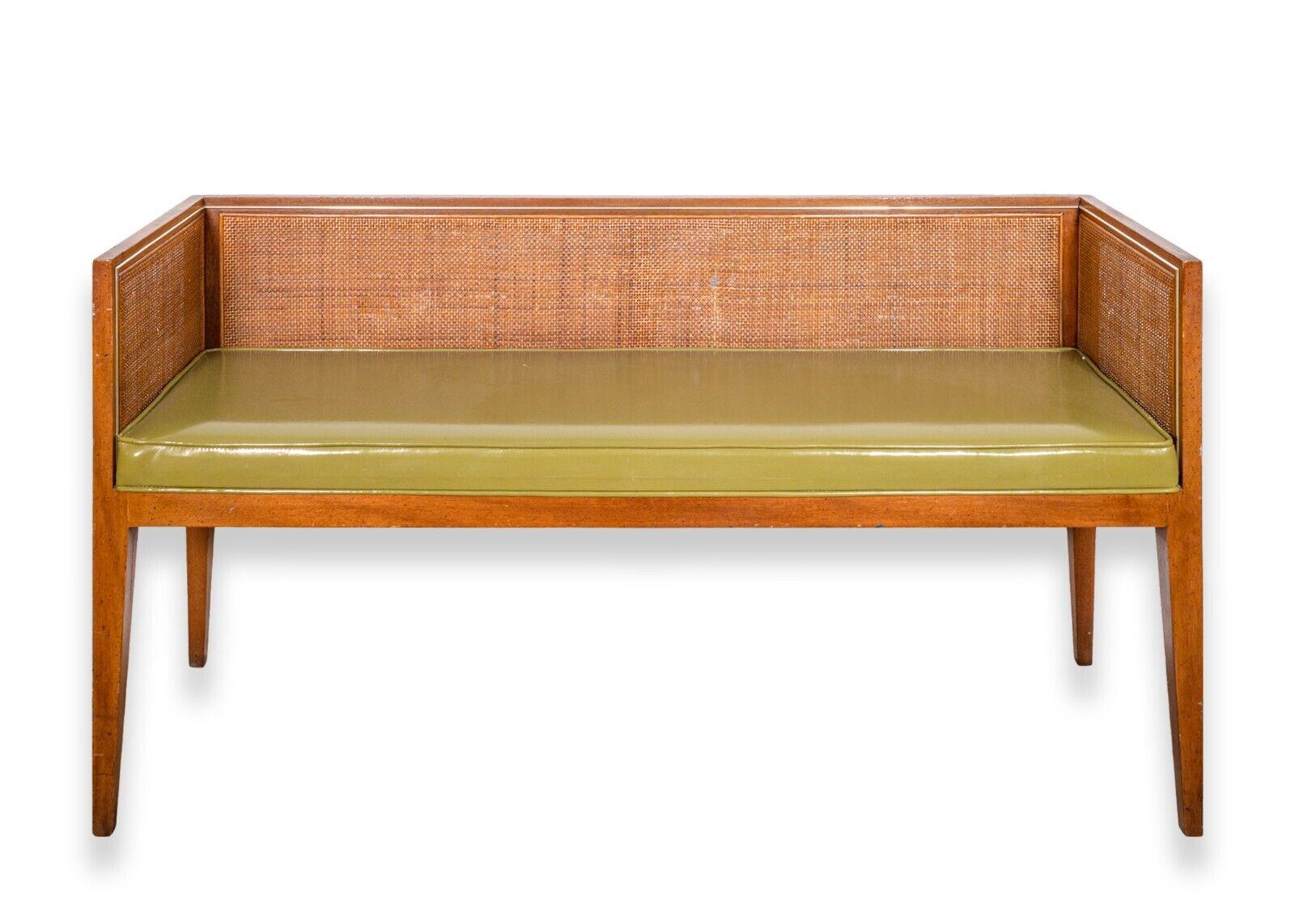 A Baker mid century modern wood and cane green Naugahyde bench. This very pretty bench features a very clean rectangular design with hairpin legs, a shiny green leather seat, and a full wooden frame construction with can detailing. This piece is in