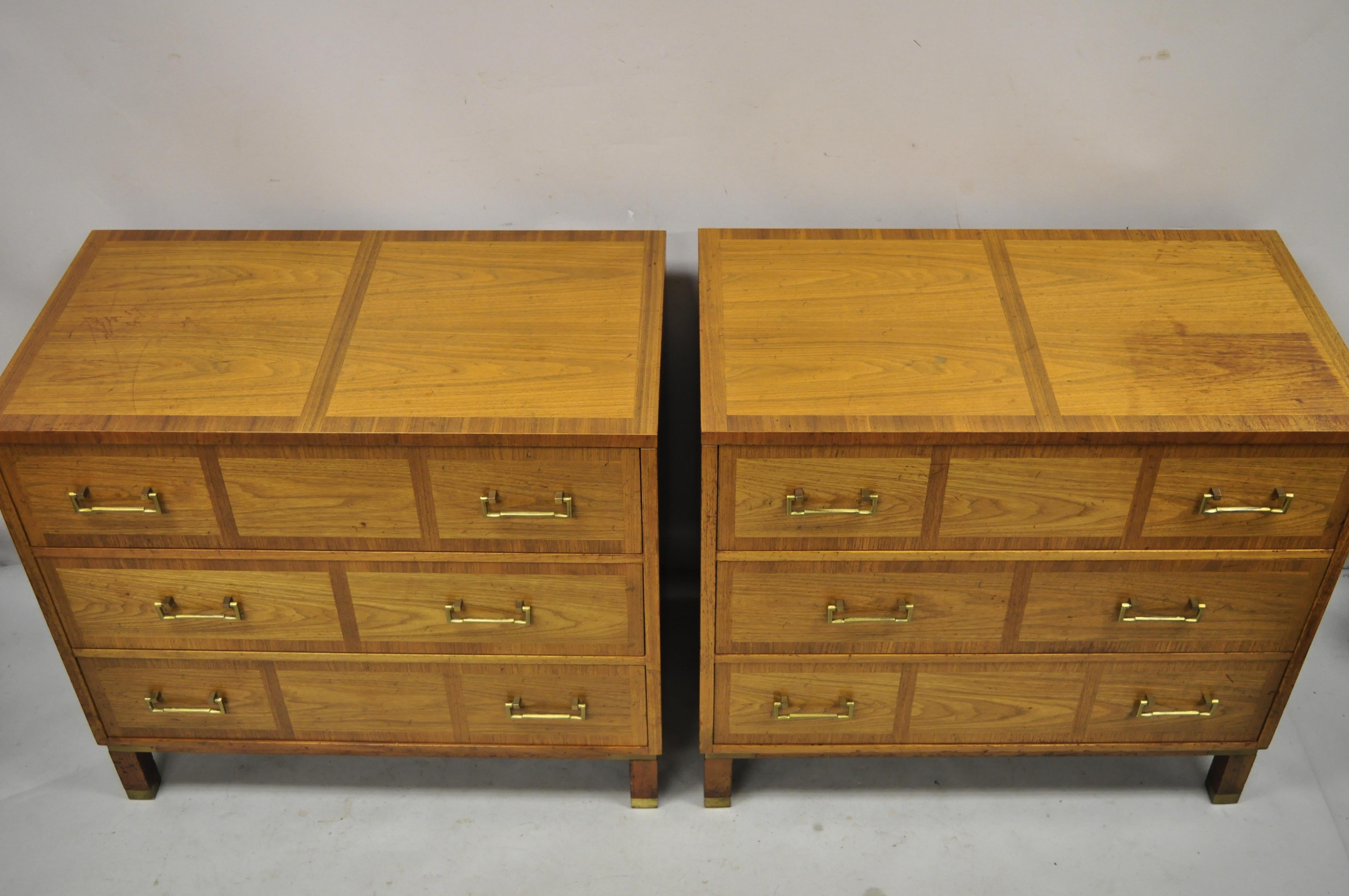 Baker milling road banded walnut brass campaign style bachelor chest dresser - a pair. Item features banded inlay drawer fronts and top, brass capped feet, beautiful wood grain, original stamp, 3 dovetailed drawers, solid brass hardware, quality
