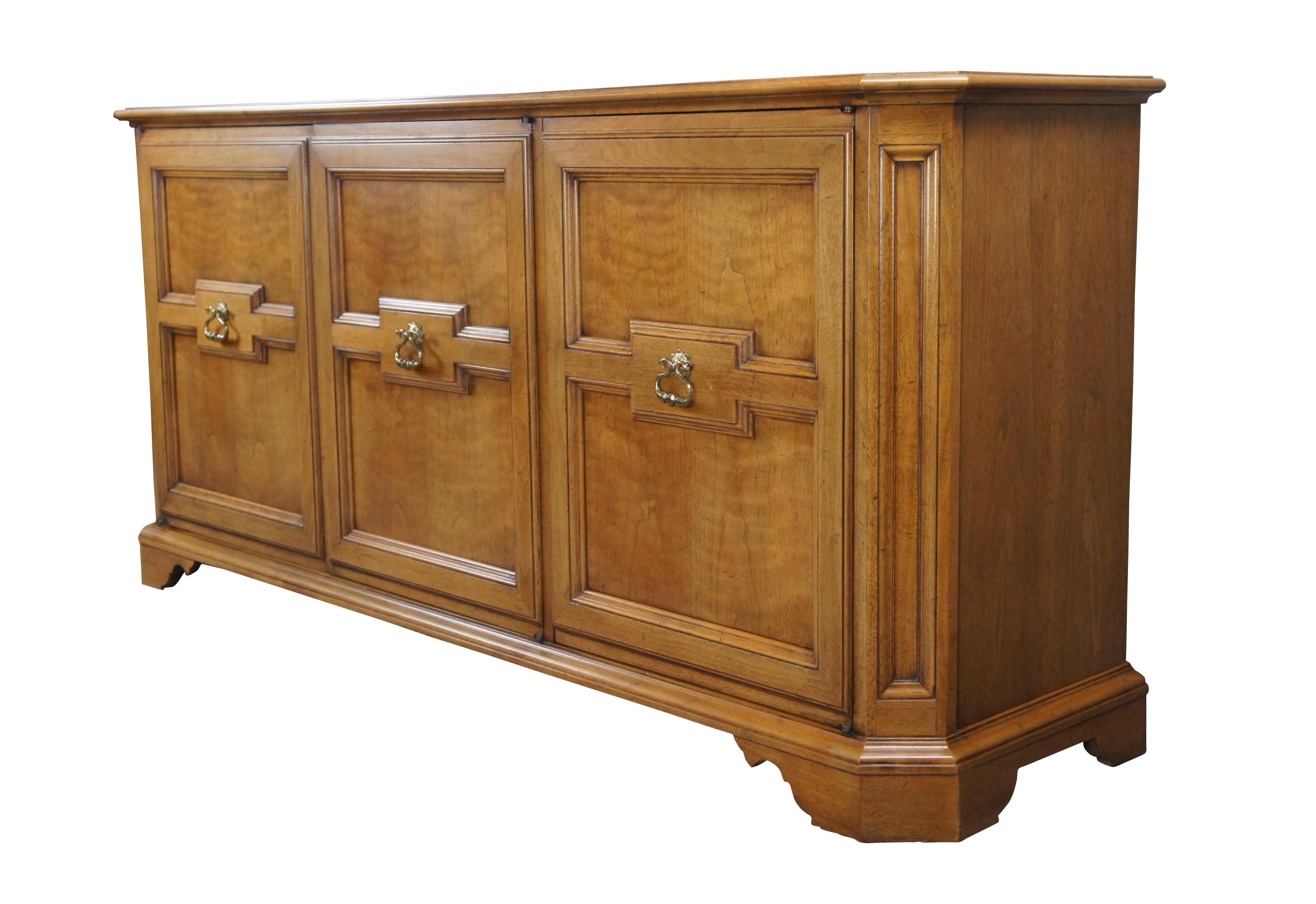 Baker Furniture Milling Road Sideboard, circa 1960s. A rectangular form made from walnut with chamfered corners. The case is fitted with 3 large doors having Italian Neoclassical and Tuscan style paneling. The cabinet opens via brass pulls to a