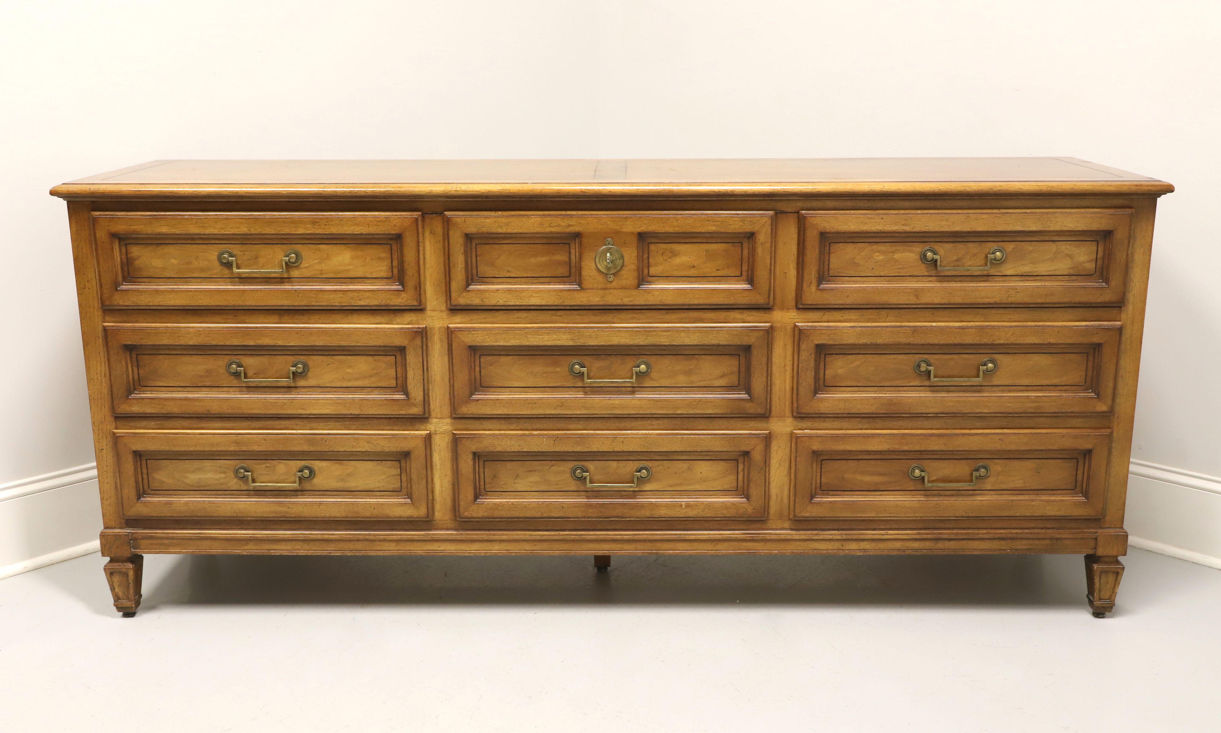 A classic Mid Century style triple dresser by Baker Furniture Company, for their Milling Road Division. Walnut with slightly distressed finish, banded top, brass hardware, raised drawer fronts and spade feet. Features nine drawers of dovetail