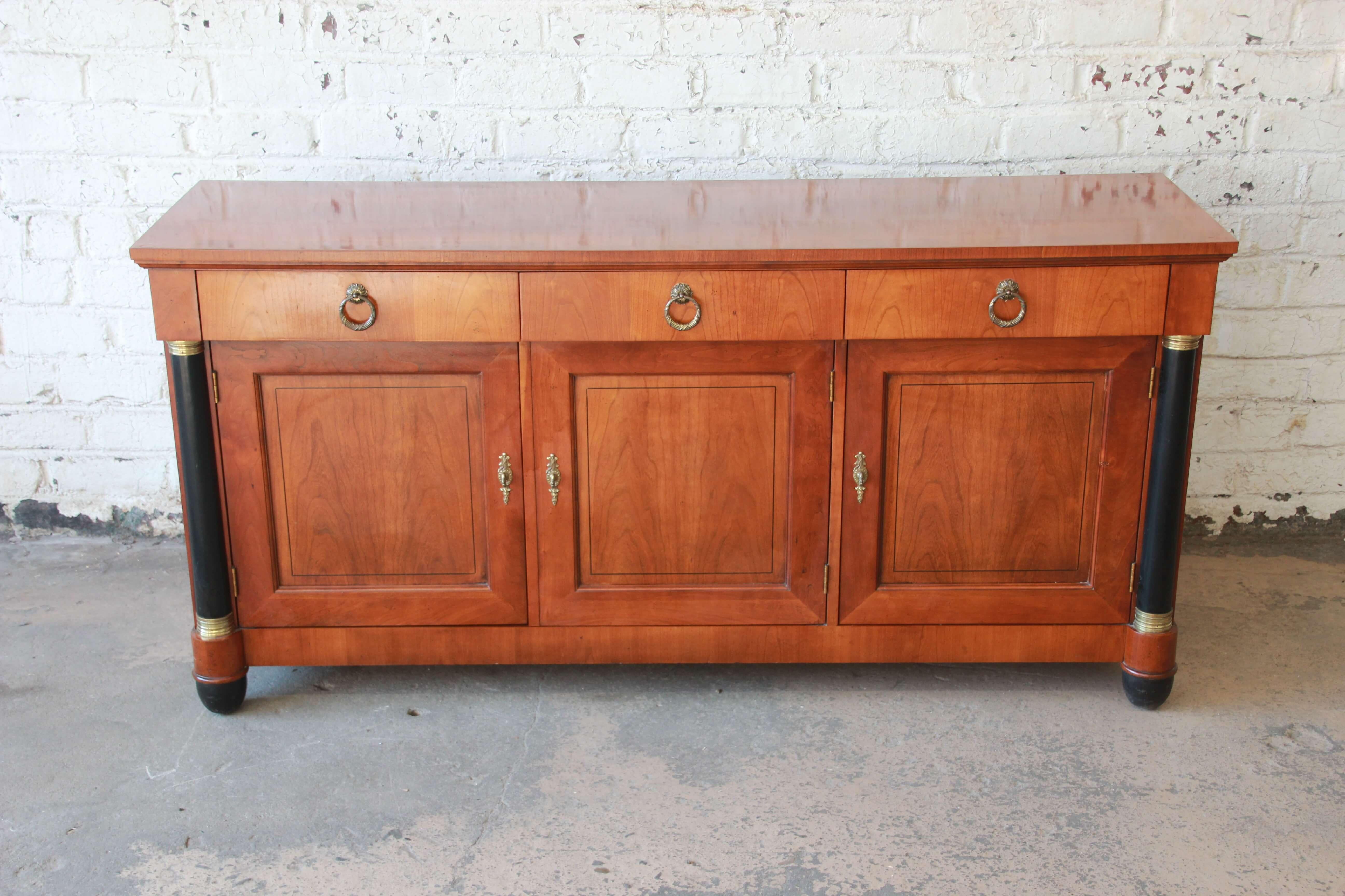 Offering a beautiful neoclassical cheerywood sideboard credenza by Baker Furniture. The piece has nice cheerywood grain with brass round pull on the top three drawers that open and close smoothly. The two cabinet doors on the left open up to a large
