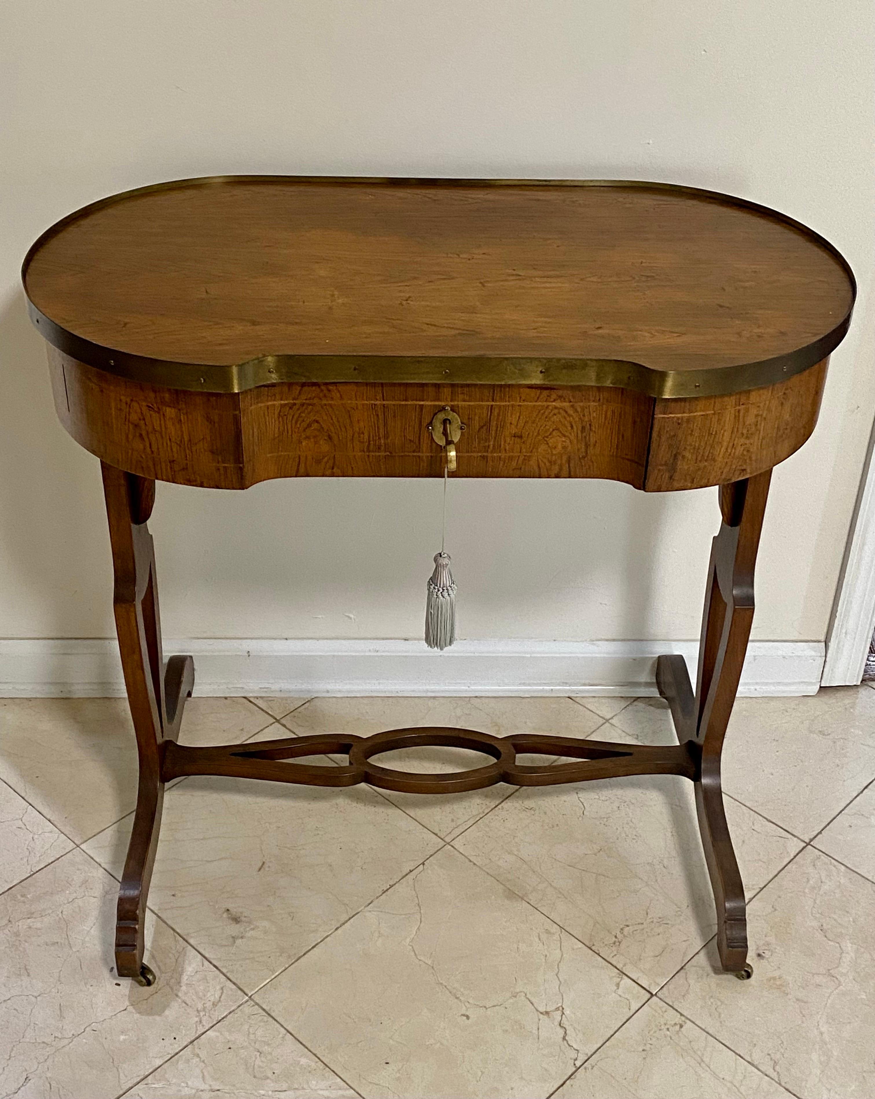 Baker Neoclassic style rosewood petite writing desk purchased from the Baker-Furniture in NYC in 1969. It is one of the pieces Baker selected for their Manor House line of Eighteenth Century style English furniture. Oblong in shape with brass trim