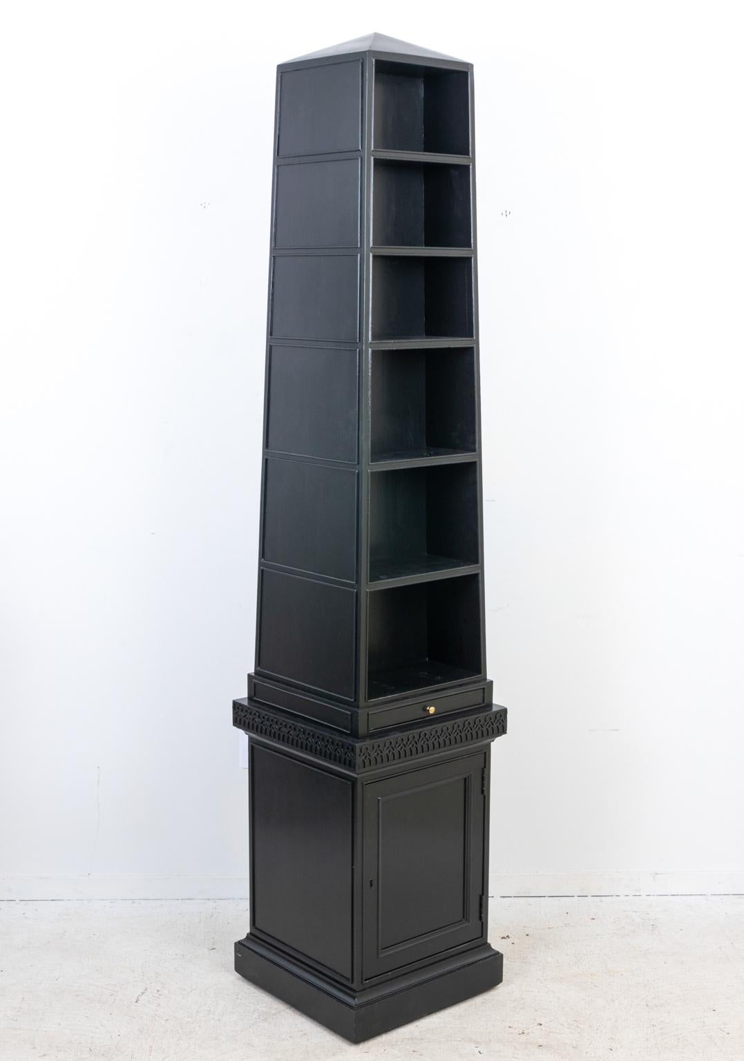 Circa 1980s pyramid or obelisk form bookcase by Baker Furniture with six shelves on the front and back. The piece also features a bottom cabinet with working key, single pull out drawer at the base of the obelisk, and fretwork detail on moldings.