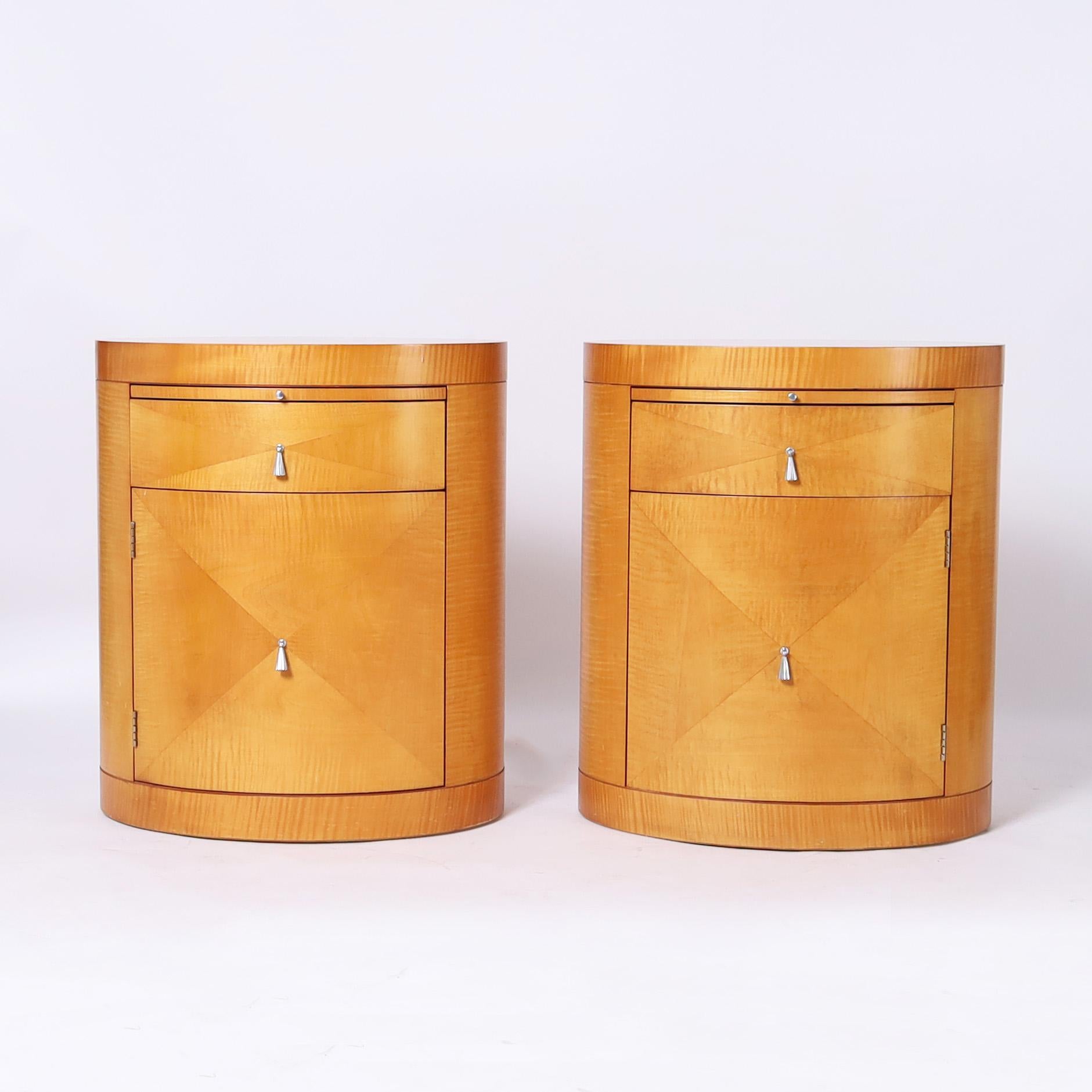Impressive pair of vintage art deco inspired stands or tables crafted in satinwood in an oval drum form with a pullout tray over a drawer and cabinet door. Signed Baker silver label in a drawer.