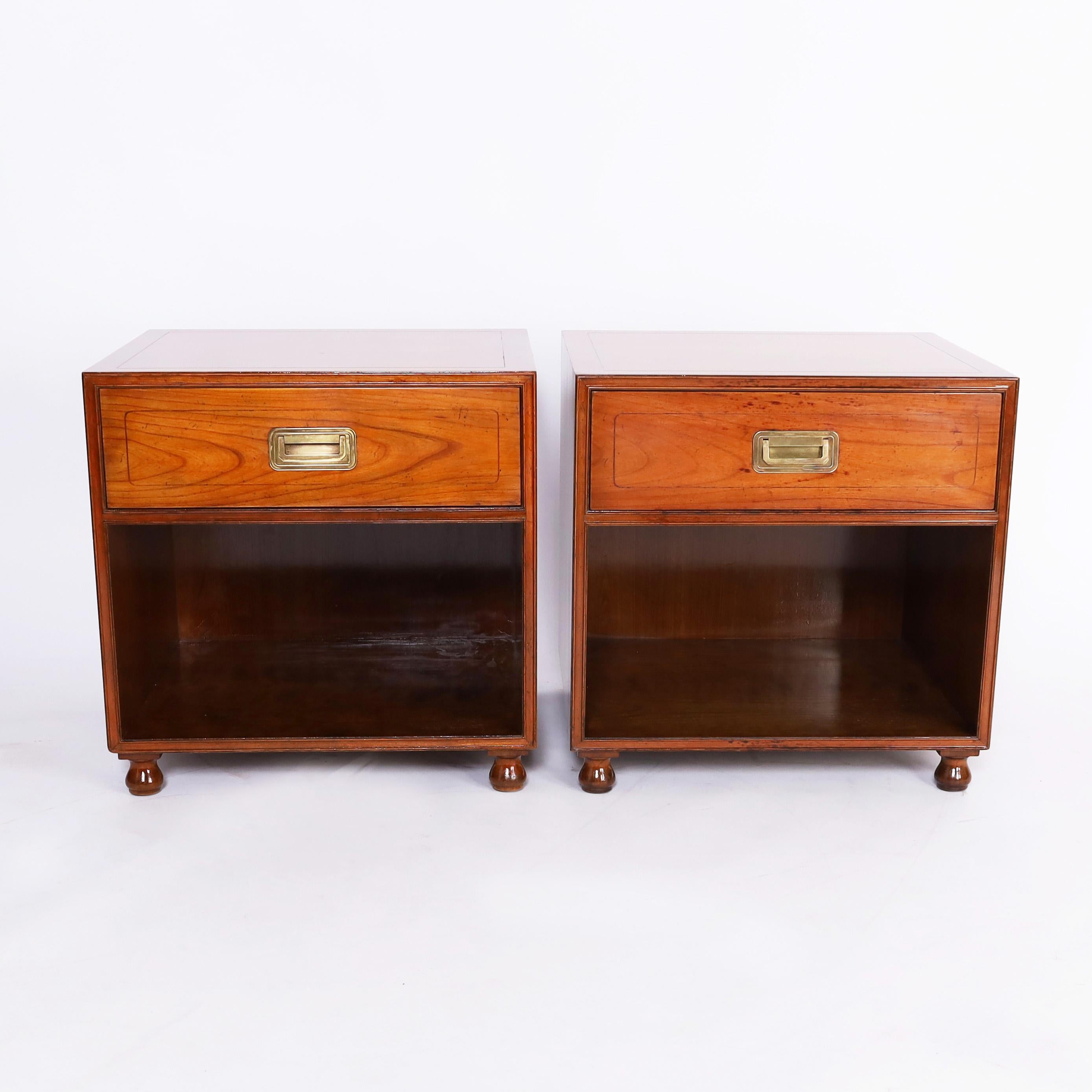 Mid century pair of stands crafted in fruitwood in a modern form with campaign hardware, one drawer, lower storage, and turned feet. Signed Baker in a drawer. 