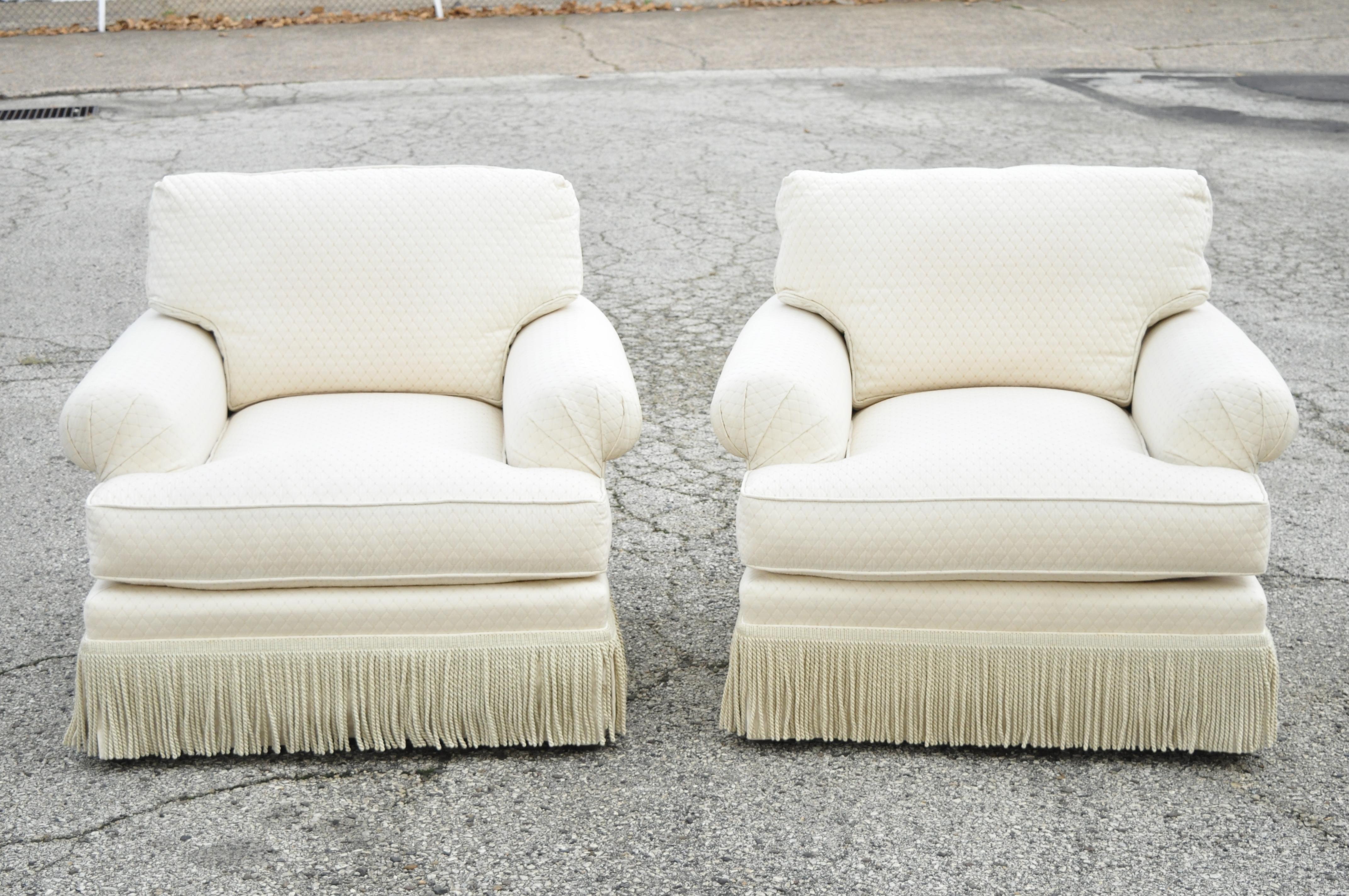 Baker custom rolled arm fringe skirt cream upholstered club lounge art deco chairs - a pair. Item features rolled and pleated arm, fringe skirt, cream/beige colored fabric with small squares, loose cushions, solid wood frames, original label,